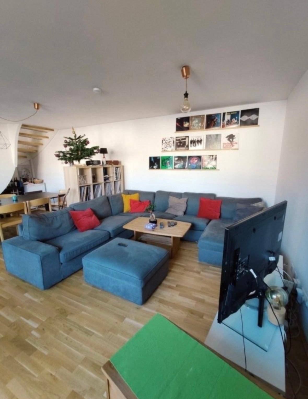 Heller Wohnbereich mit großem Ecksofa, Fernseher und dekorativen Elementen an der Wand.