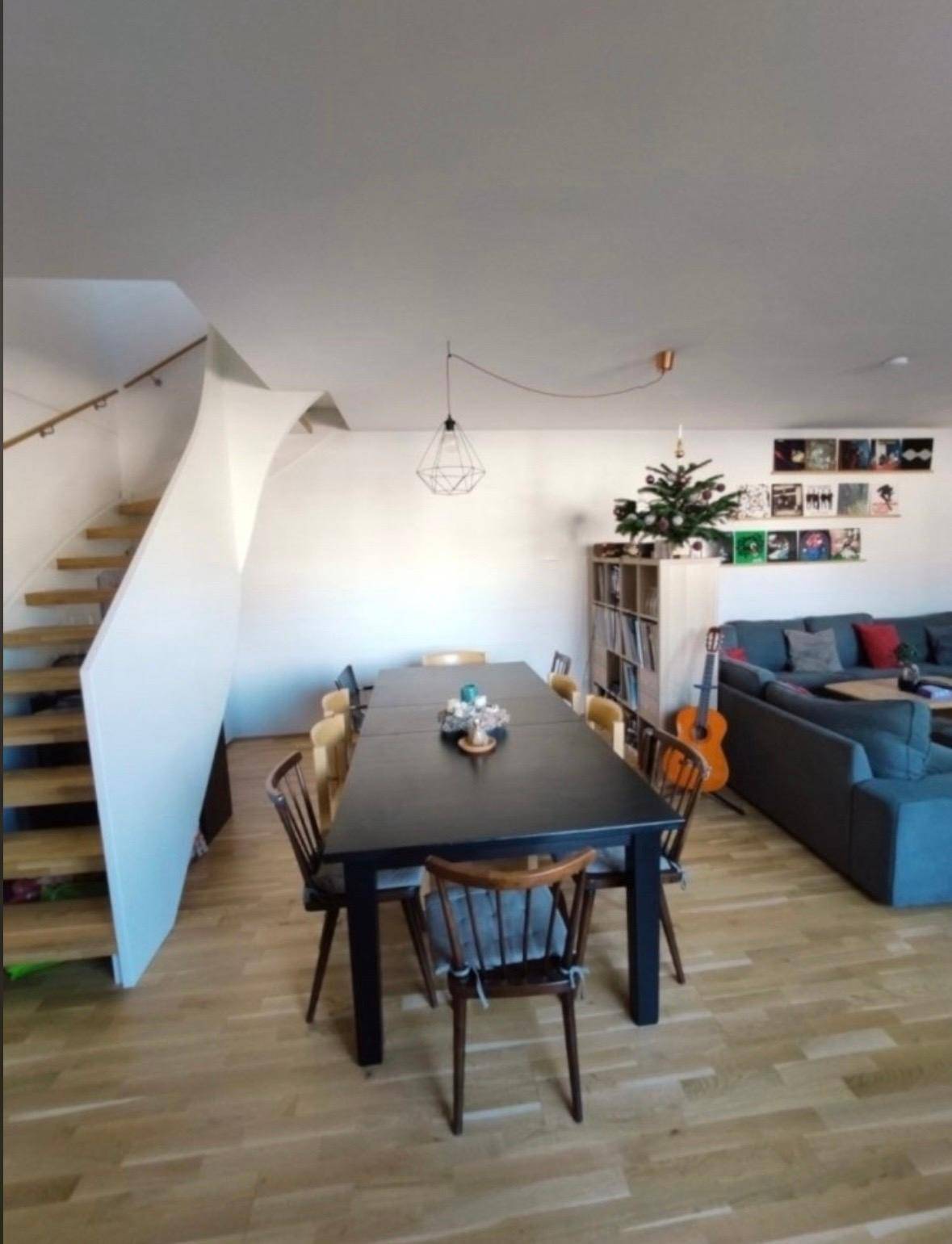 Heller Wohn- und Essbereich mit Holzparkett, einer modernen Treppe und gemütlichem Sofa.