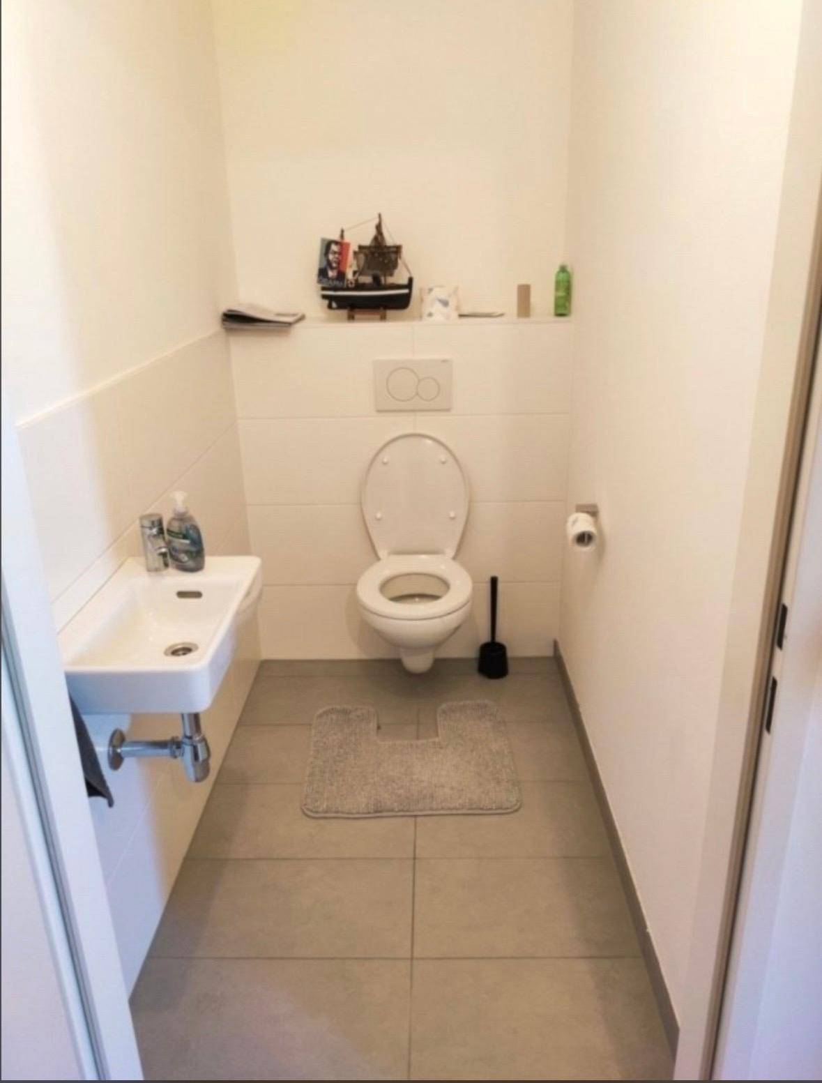 Modernes Gäste-WC mit Wand-WC, kleinem Waschbecken und grauen Fliesen.