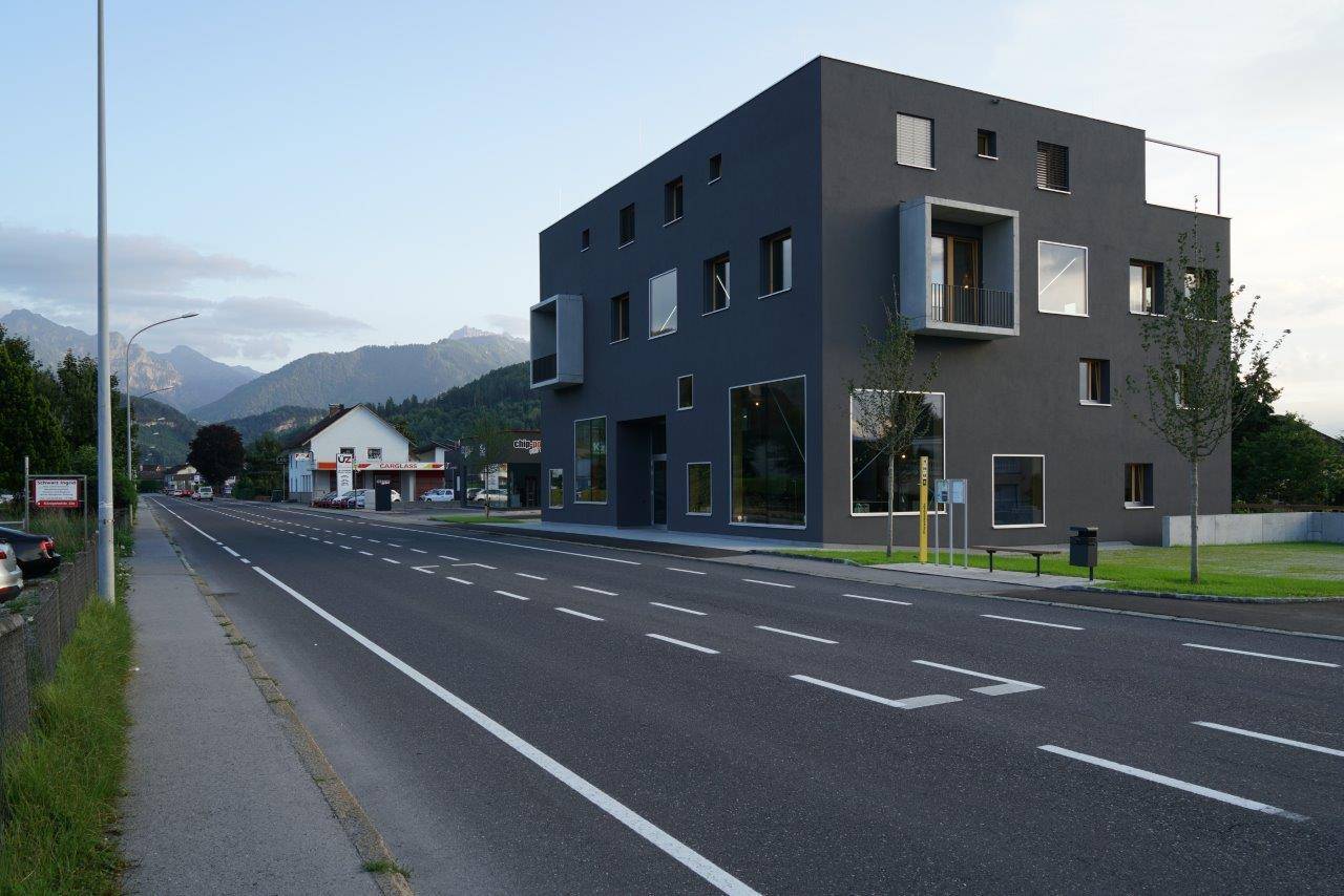 Modernes, dunkles Gebäude mit markanter Architektur und großen Fenstern an einer Straße gelegen.