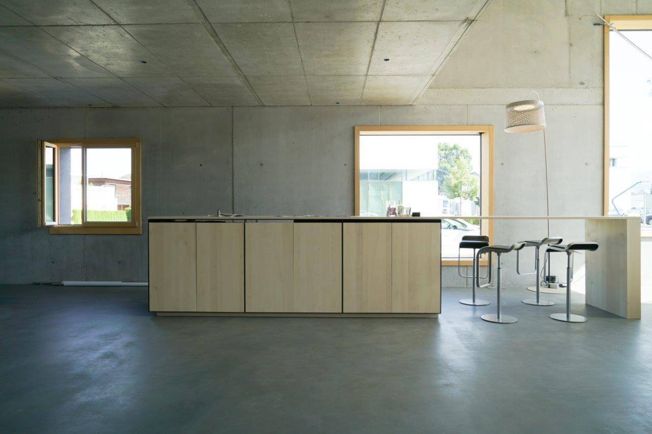 Moderne Küchenzeile mit hellen Holzfronten, Barhockern und großen Fenstern in einem offenen Raum.
