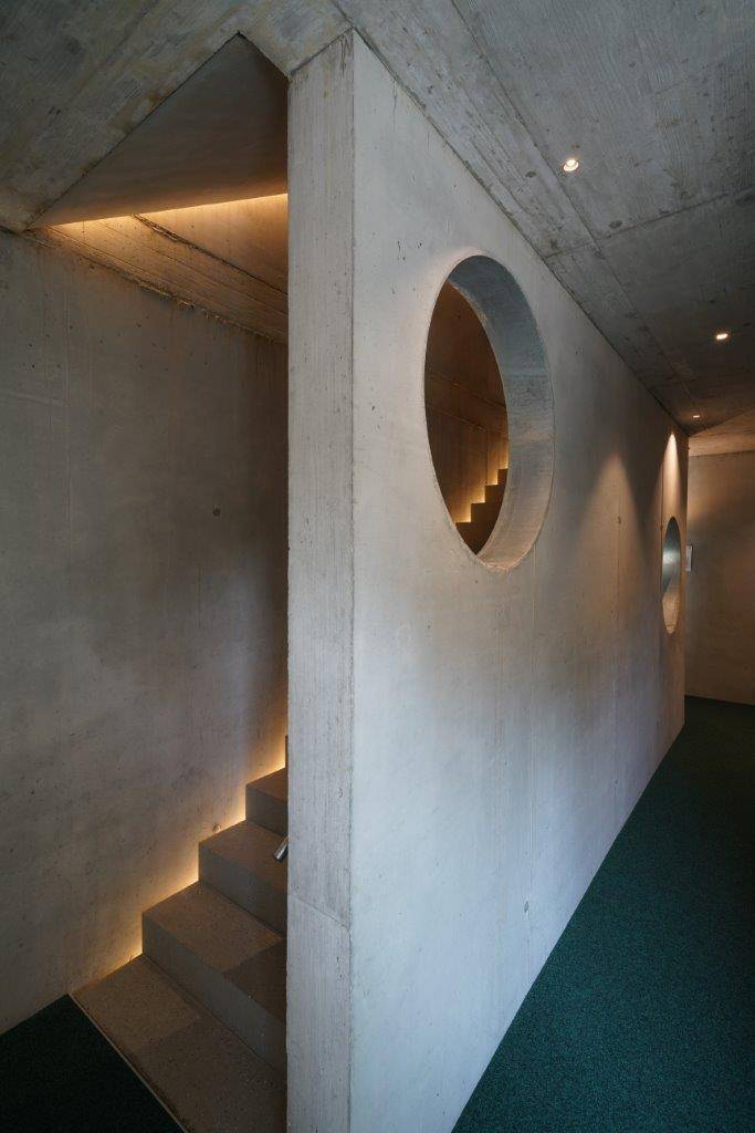 Moderner Flur mit Betontreppe, runden Wandöffnungen und stimmungsvoller indirekter Beleuchtung.