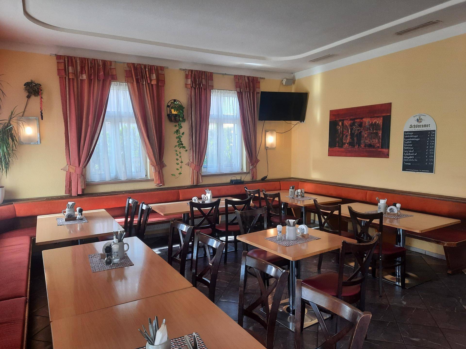 Gemütlicher Restaurant-Essbereich mit traditionellen Holztischen, gepolsterten Bänken und dekorativen Vorhängen.
