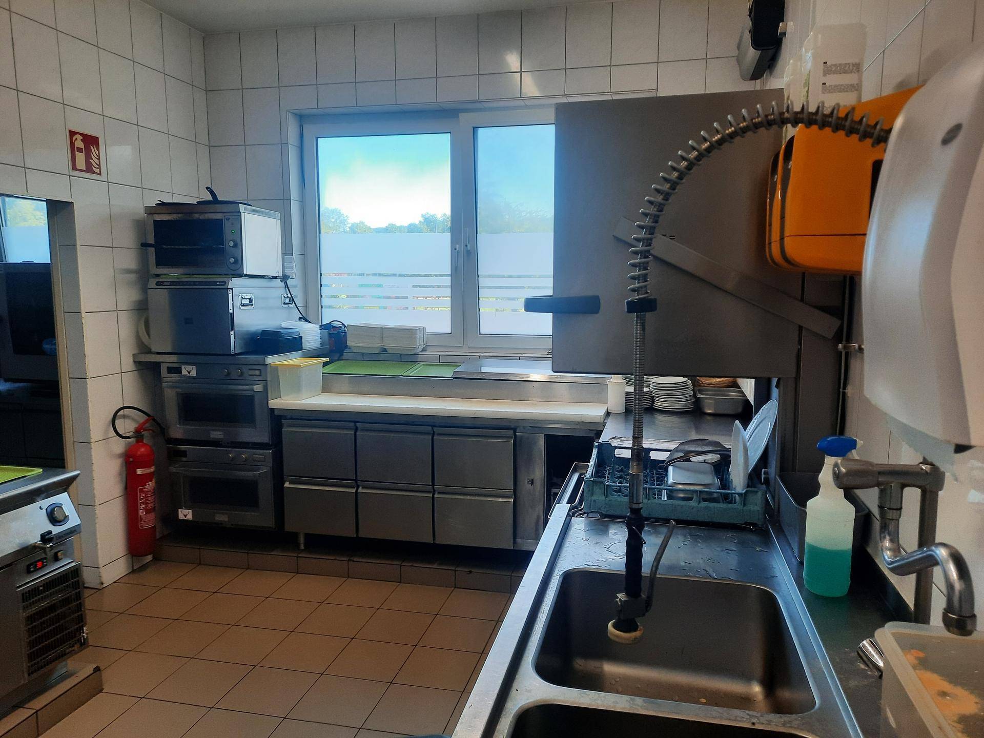 Spülbereich einer Großküche mit Doppelwaschbecken, professioneller Armatur und großem Fenster.