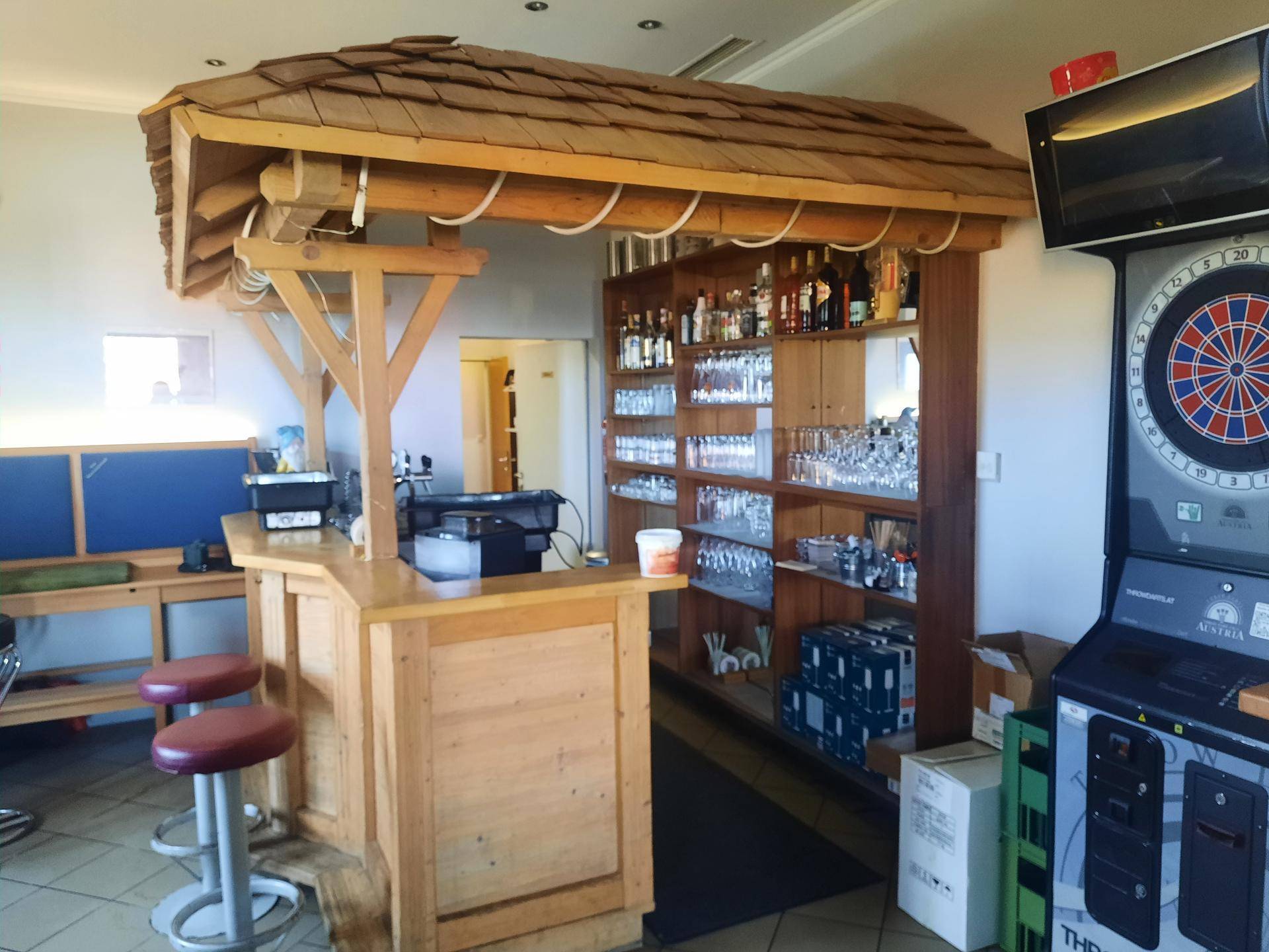 Helle Bar mit rustikalem Holzdach, Barhockern und einer gut bestückten Getränkeauslage.