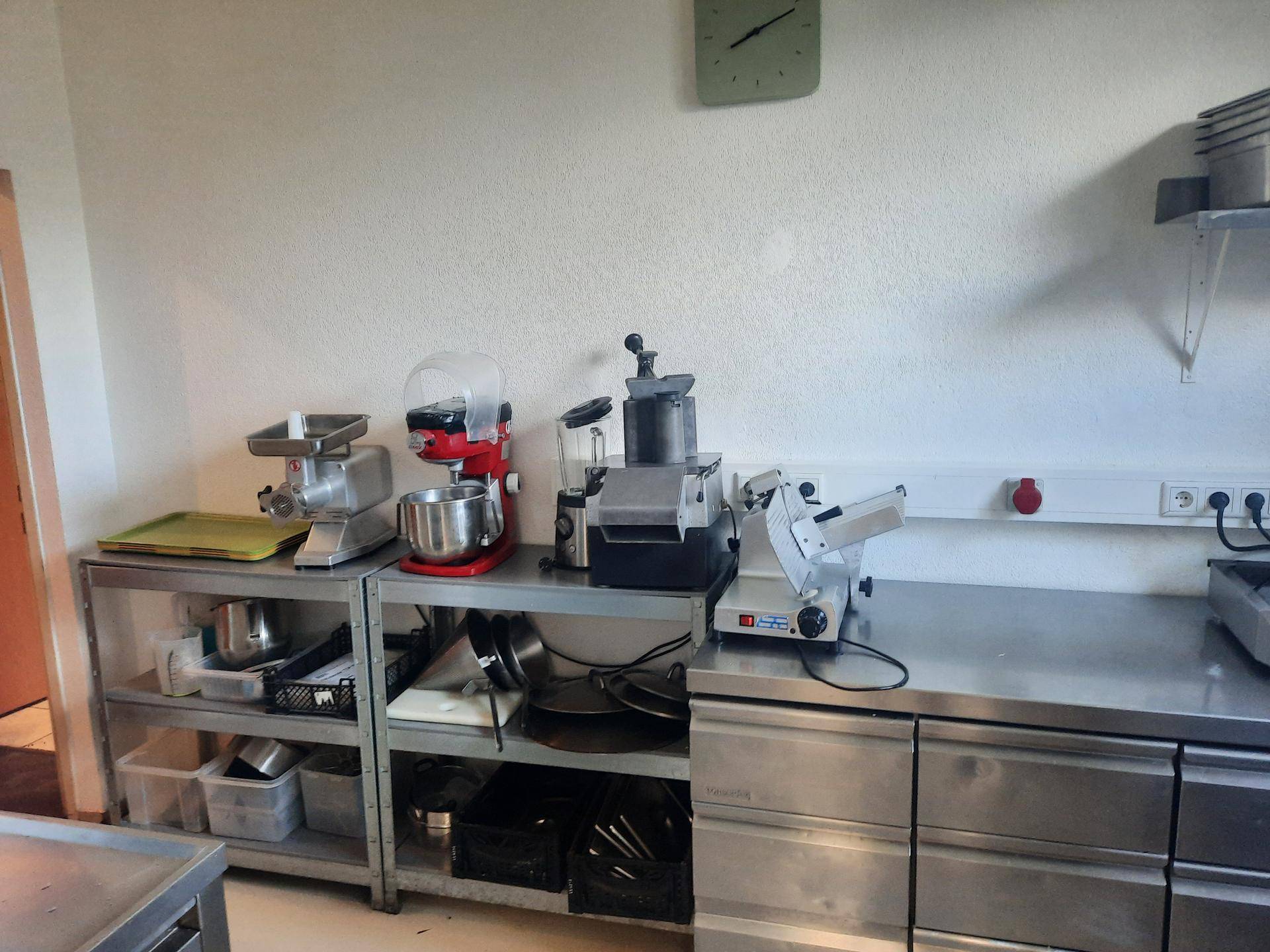 Küchenarbeitsbereich mit Edelstahlregalen, verschiedenen Küchengeräten und einer hellen Wand.