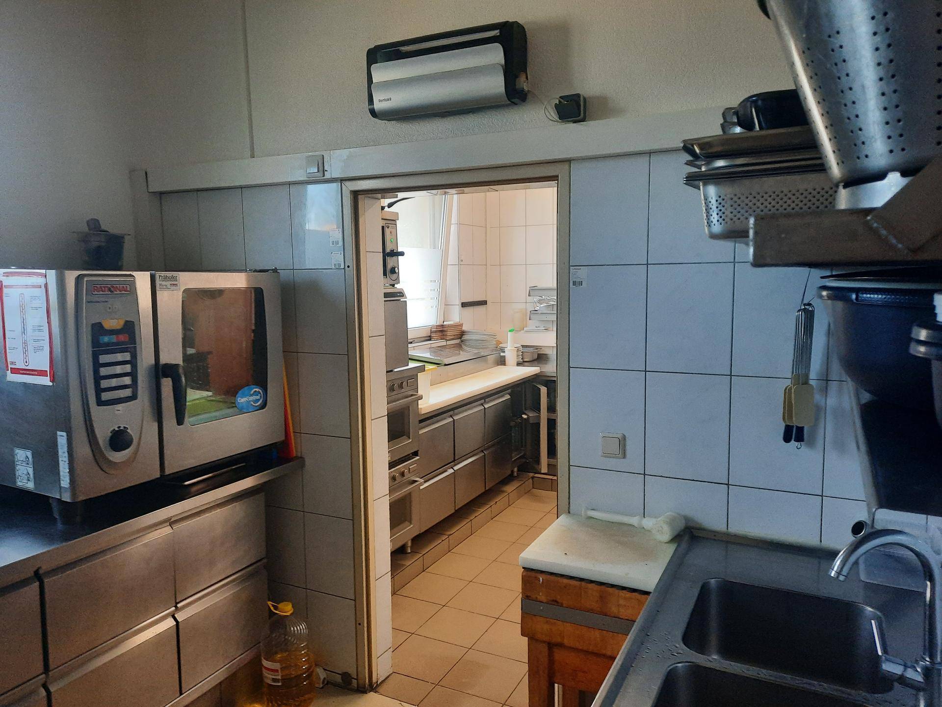 Teil einer professionellen Küche mit großem Ofen und Durchgang zu einem weiteren Küchenbereich.