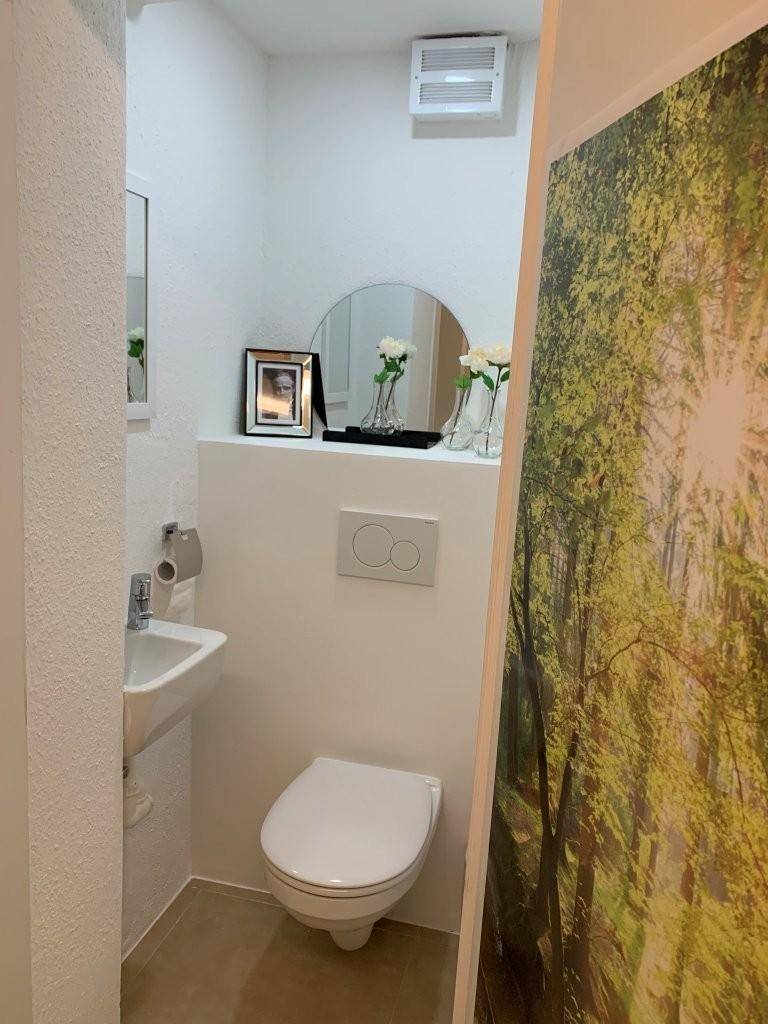 Modernes Gäste-WC mit wandhängender Toilette, kleinem Waschbecken und Waldmotiv-Tapete.