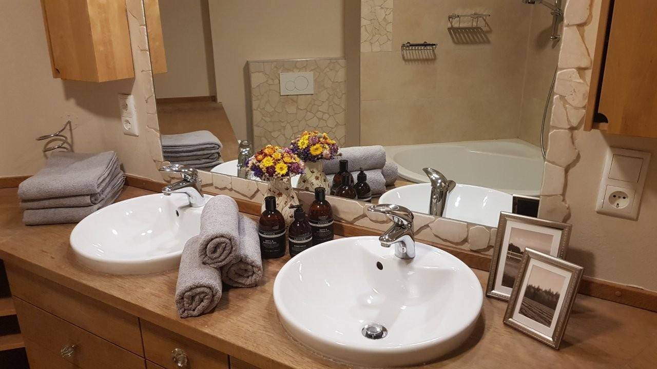Geräumiges Badezimmer mit Doppelwaschbecken, großem Spiegel und Badewanne im Hintergrund.