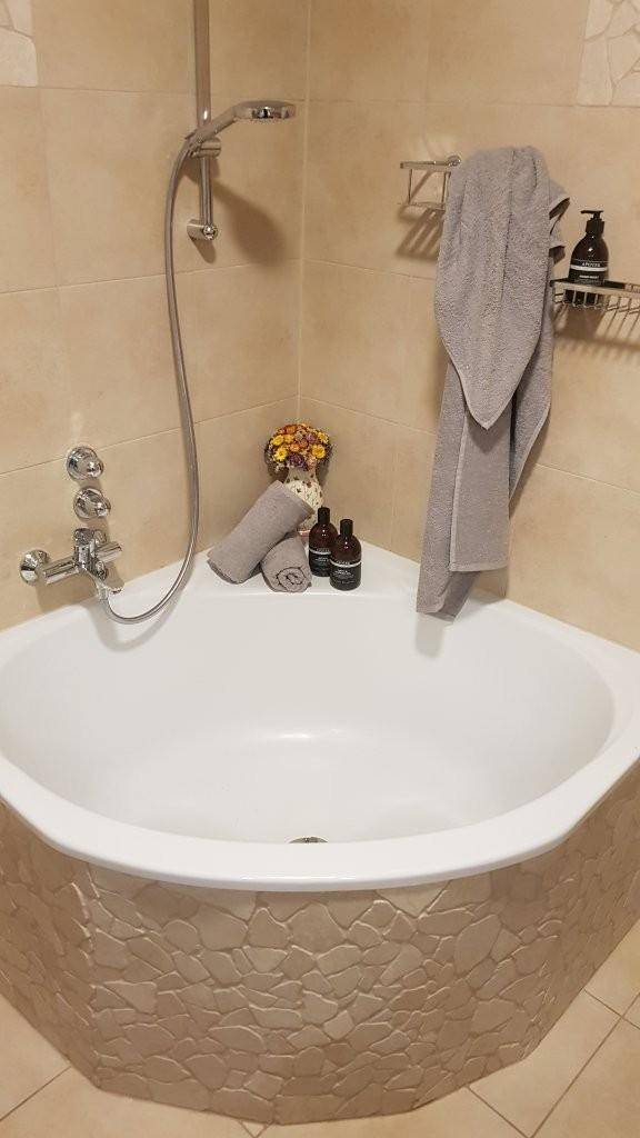 Eckbadewanne mit integrierter Duschfunktion und beigefarbenen Fliesen.