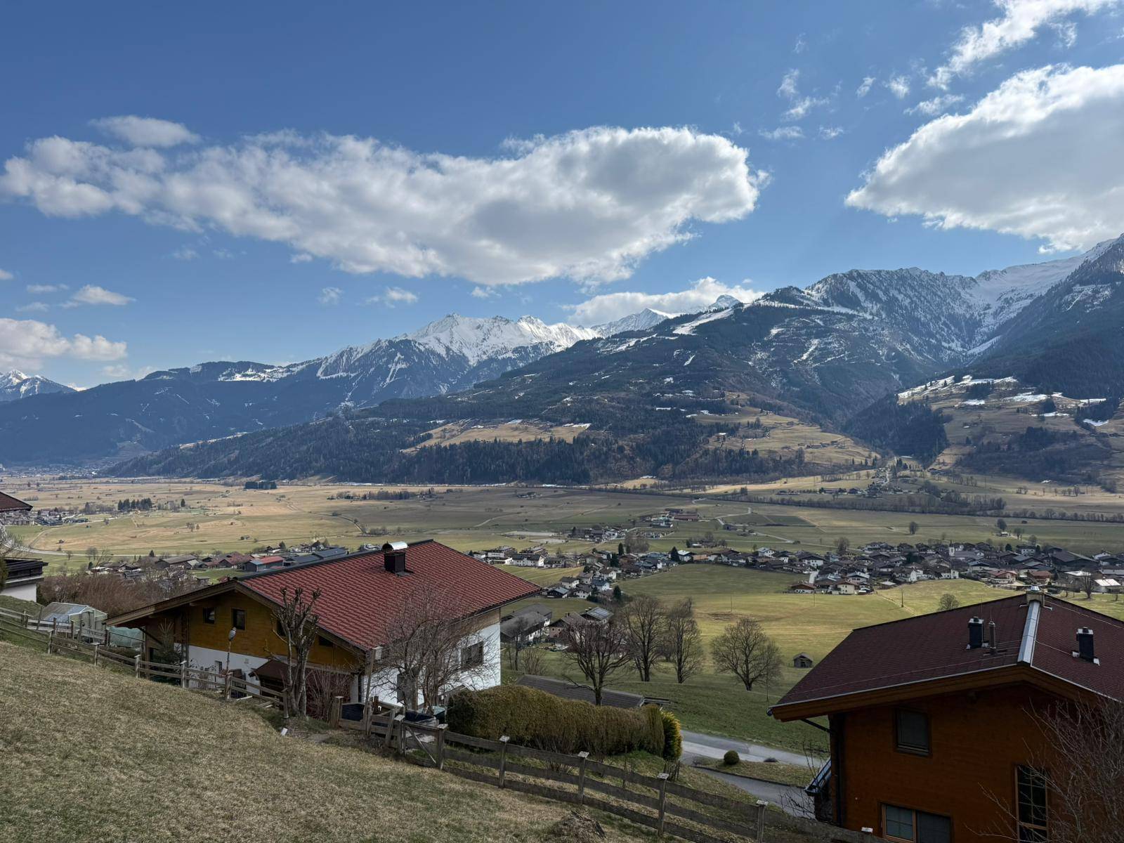 Sonniger Blick über eine ländliche Landschaft mit Wohnhäusern und einer beeindruckenden Bergkulisse.