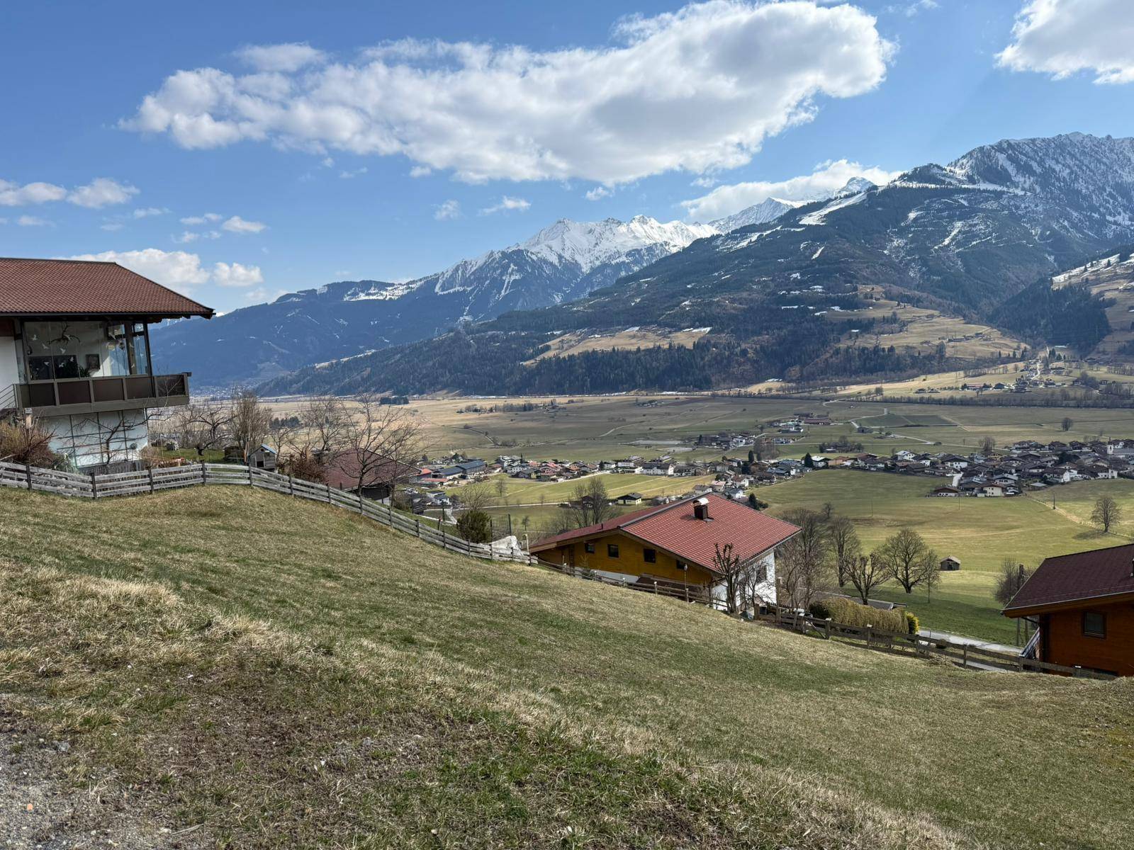 Malerischer Ausblick auf ein grünes Tal mit verstreuten Häusern und majestätischen Bergen im Hintergrund.