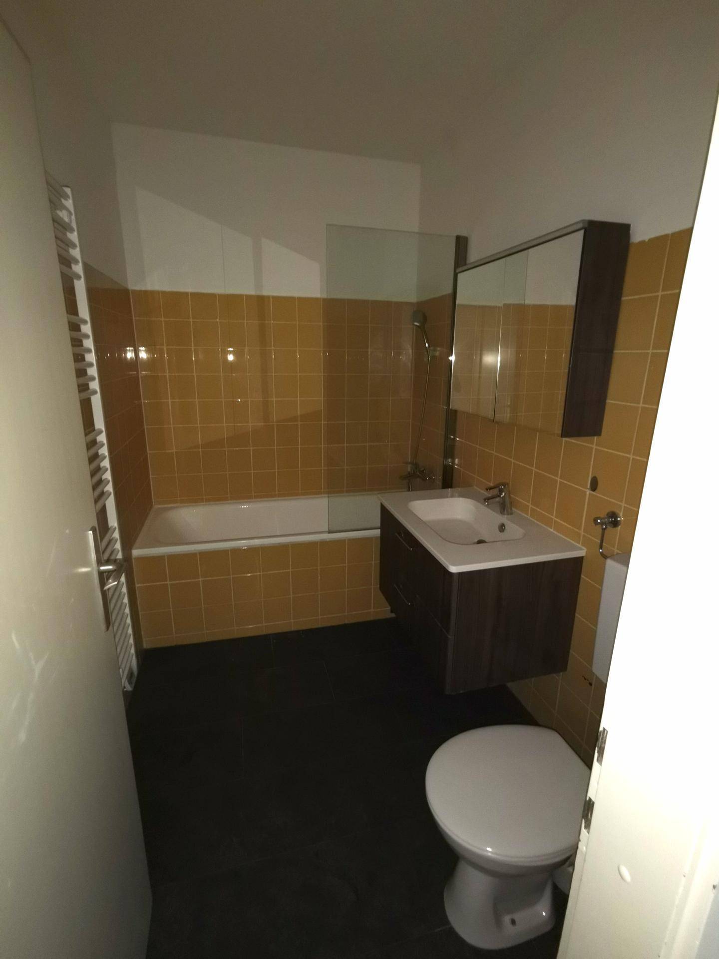 Badezimmer mit Badewanne, Waschbecken und WC, ausgestattet mit gelben Wandfliesen und einem Handtuchheizkörper.
