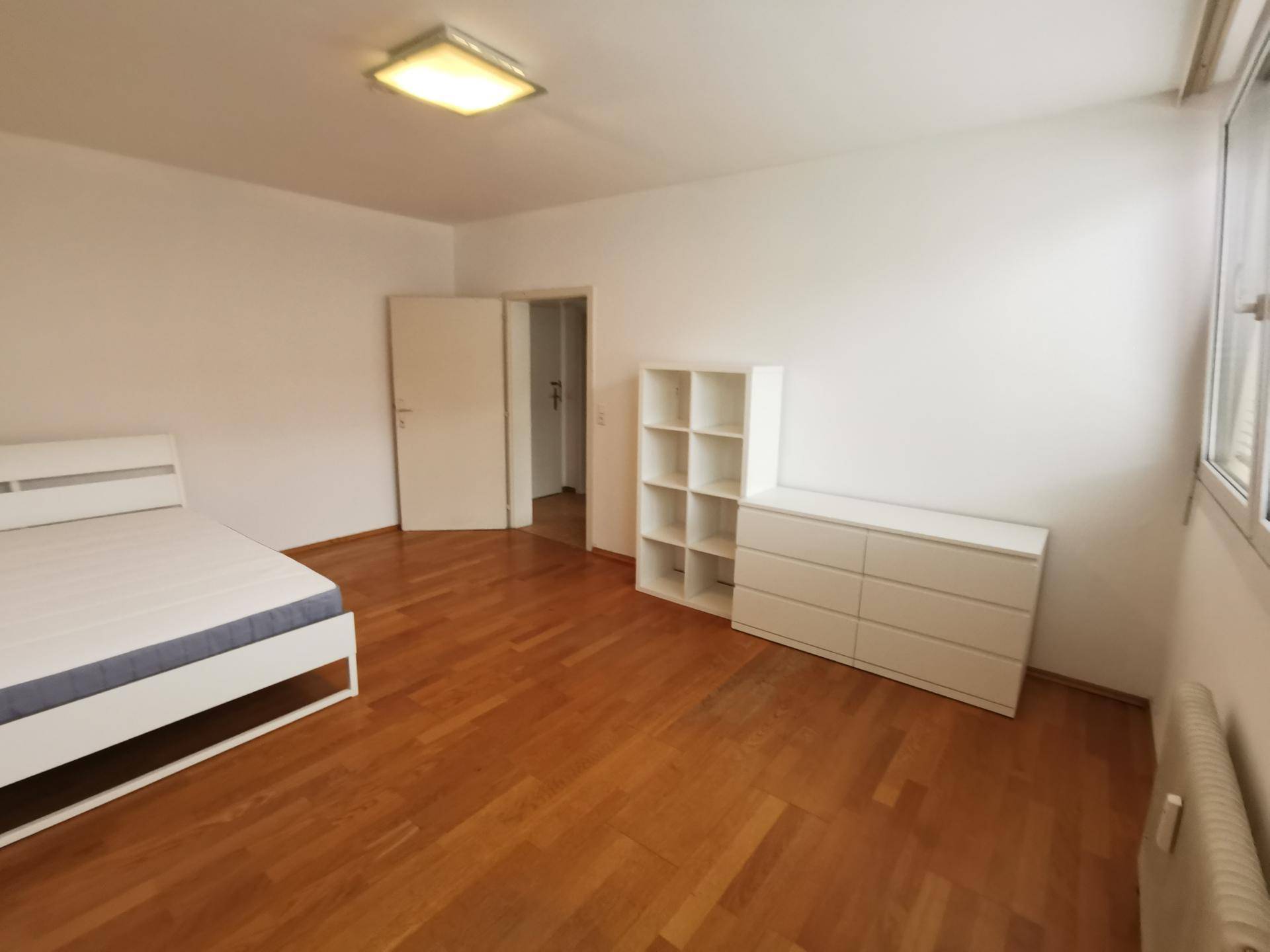 Helles Schlafzimmer mit Holzboden, einem Bettgestell und weißen Möbeln, bietet viel Tageslicht.