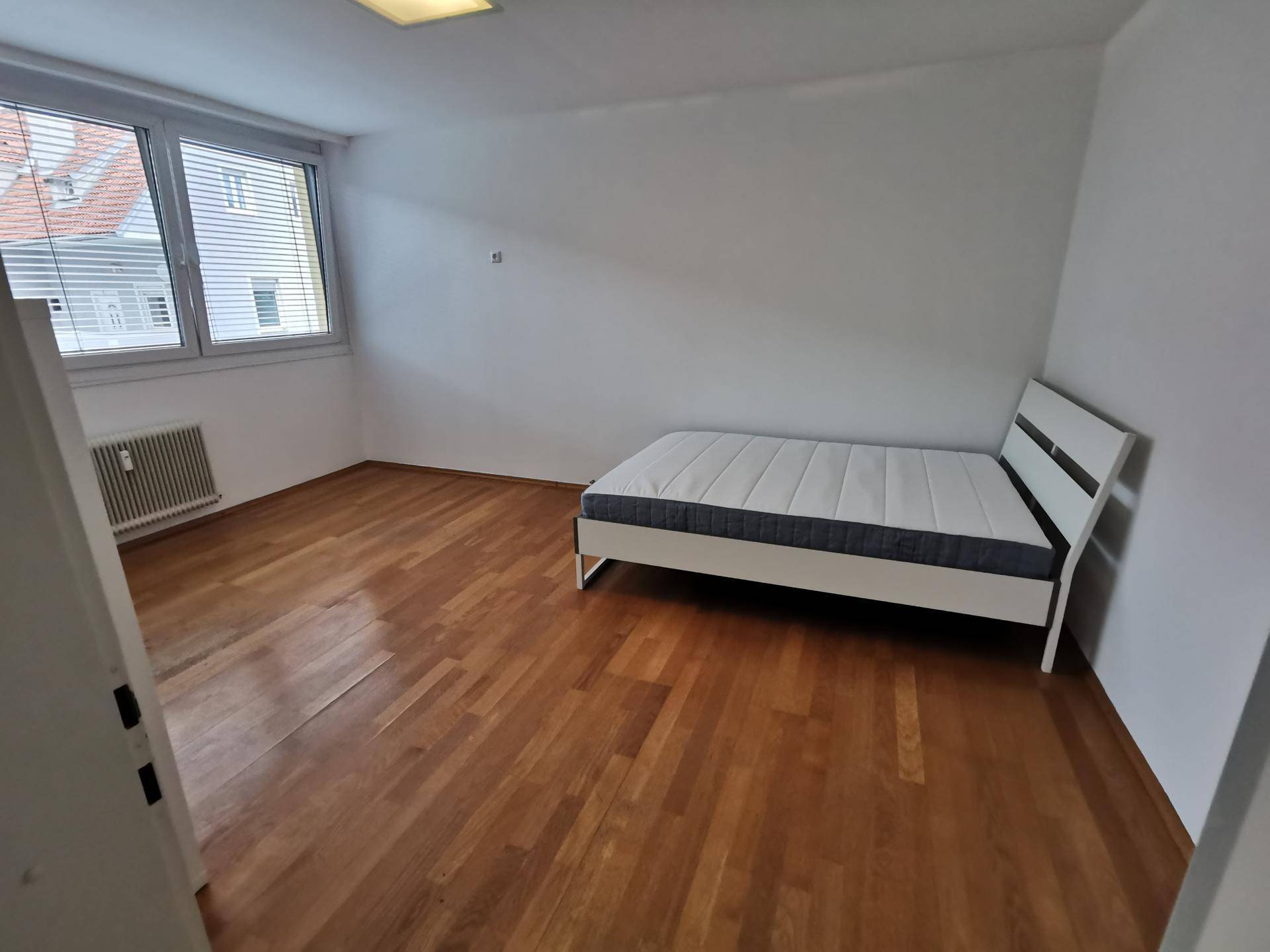 Geräumiges Schlafzimmer mit warmem Holzboden und einem großen Fenster, das viel Licht hereinlässt.