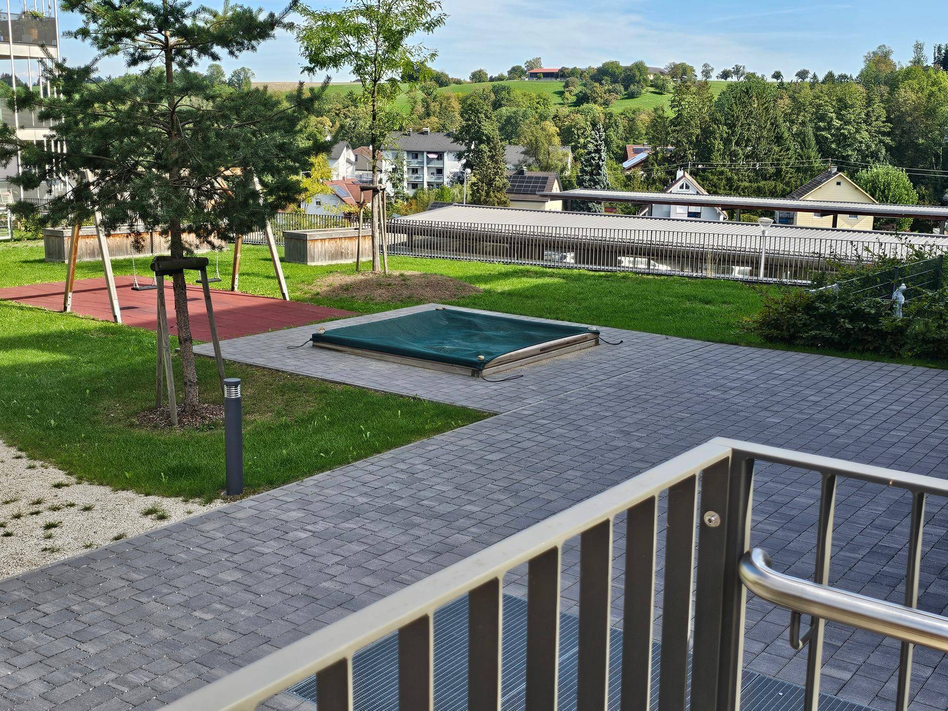 Gemeinschaftlicher Außenbereich mit Spielplatz, gepflasterten Wegen und einem abgedeckten Pool.