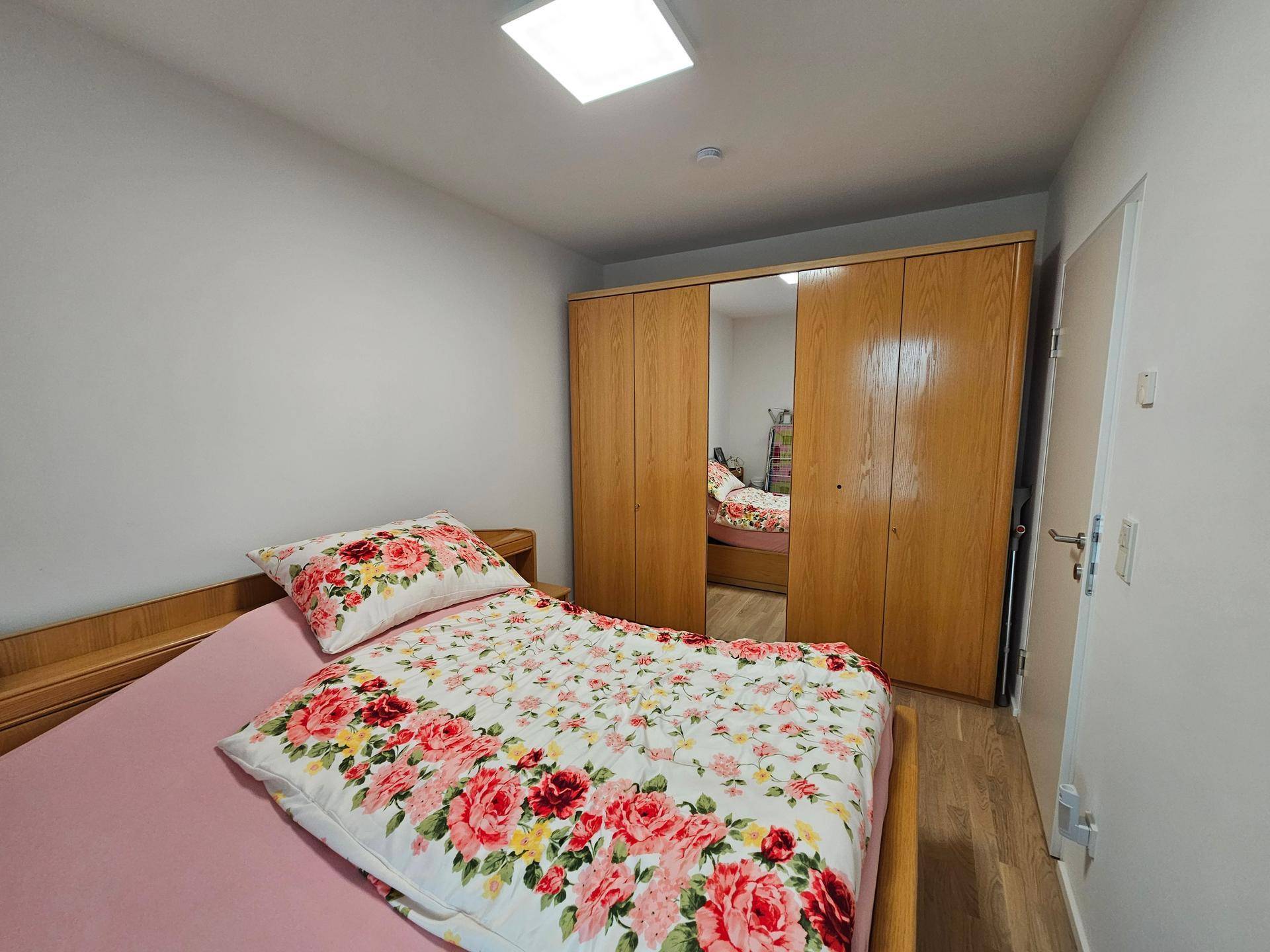 Gemütliches Schlafzimmer mit Holzbett, floraler Bettwäsche und großem Holzschrank.