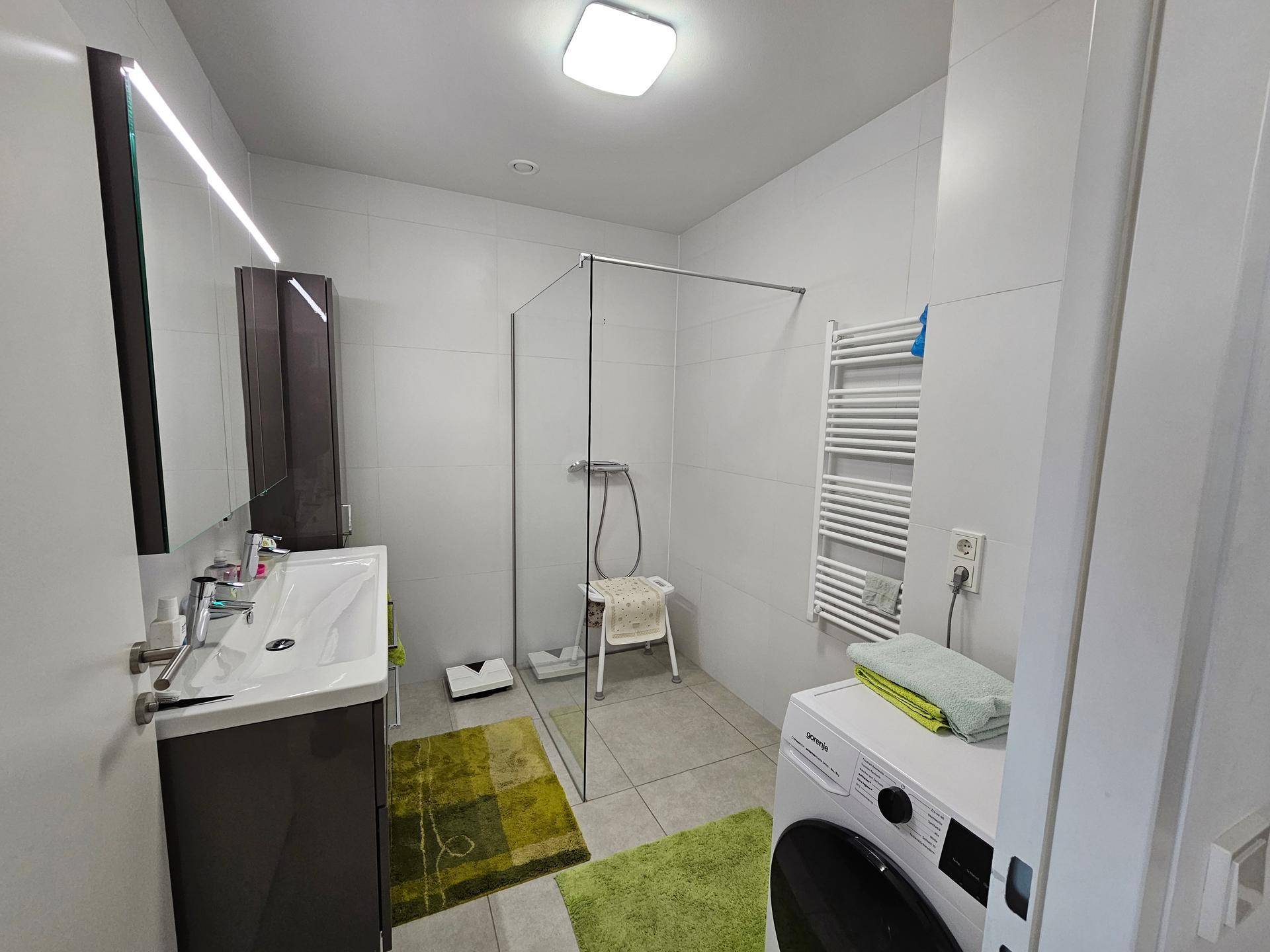 Modernes Badezimmer mit ebenerdiger Dusche, Waschbecken und Waschmaschine.