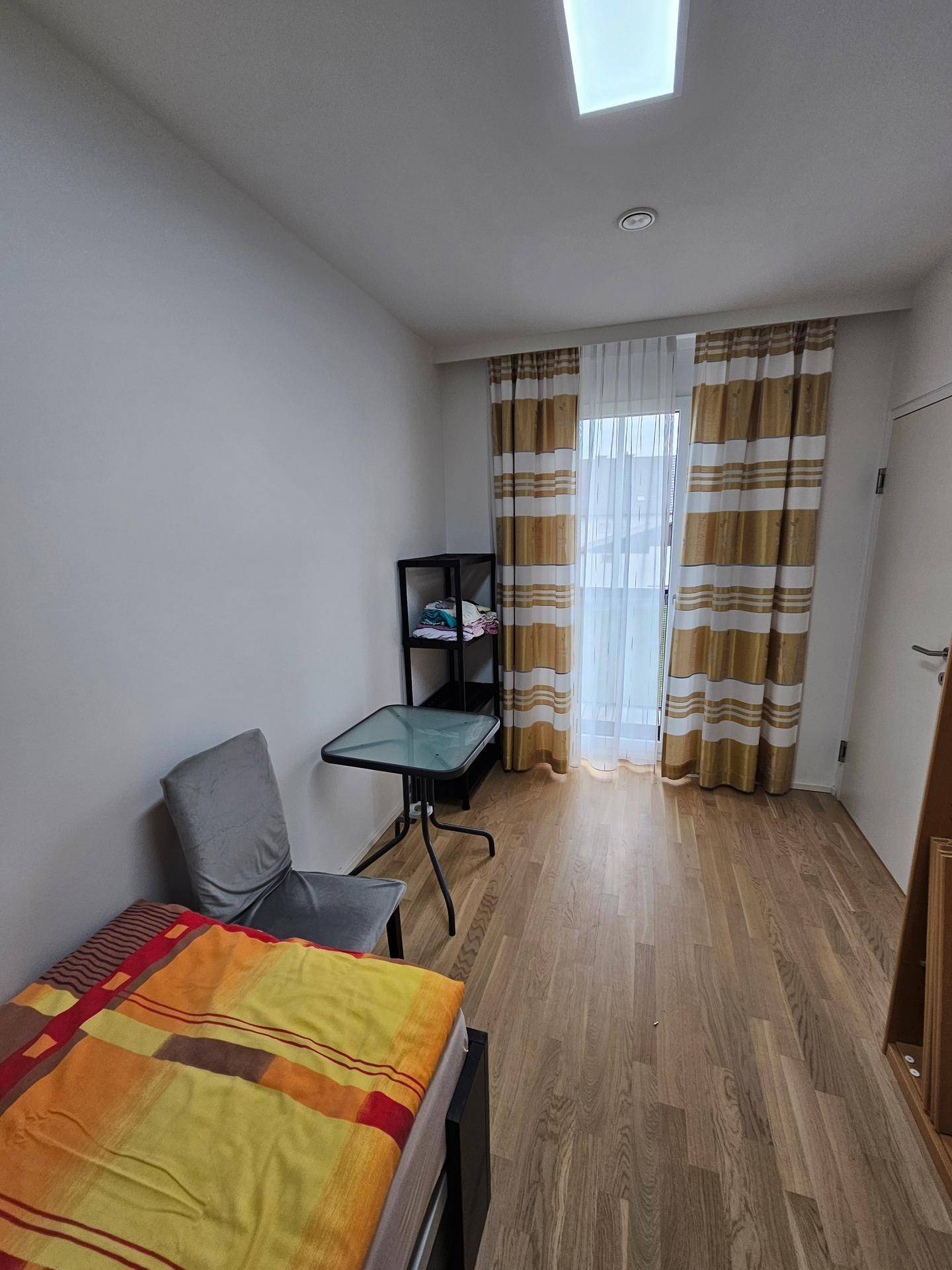 Helles Schlafzimmer mit Holzboden, Einzelbett und Zugang zu einem französischen Balkon.