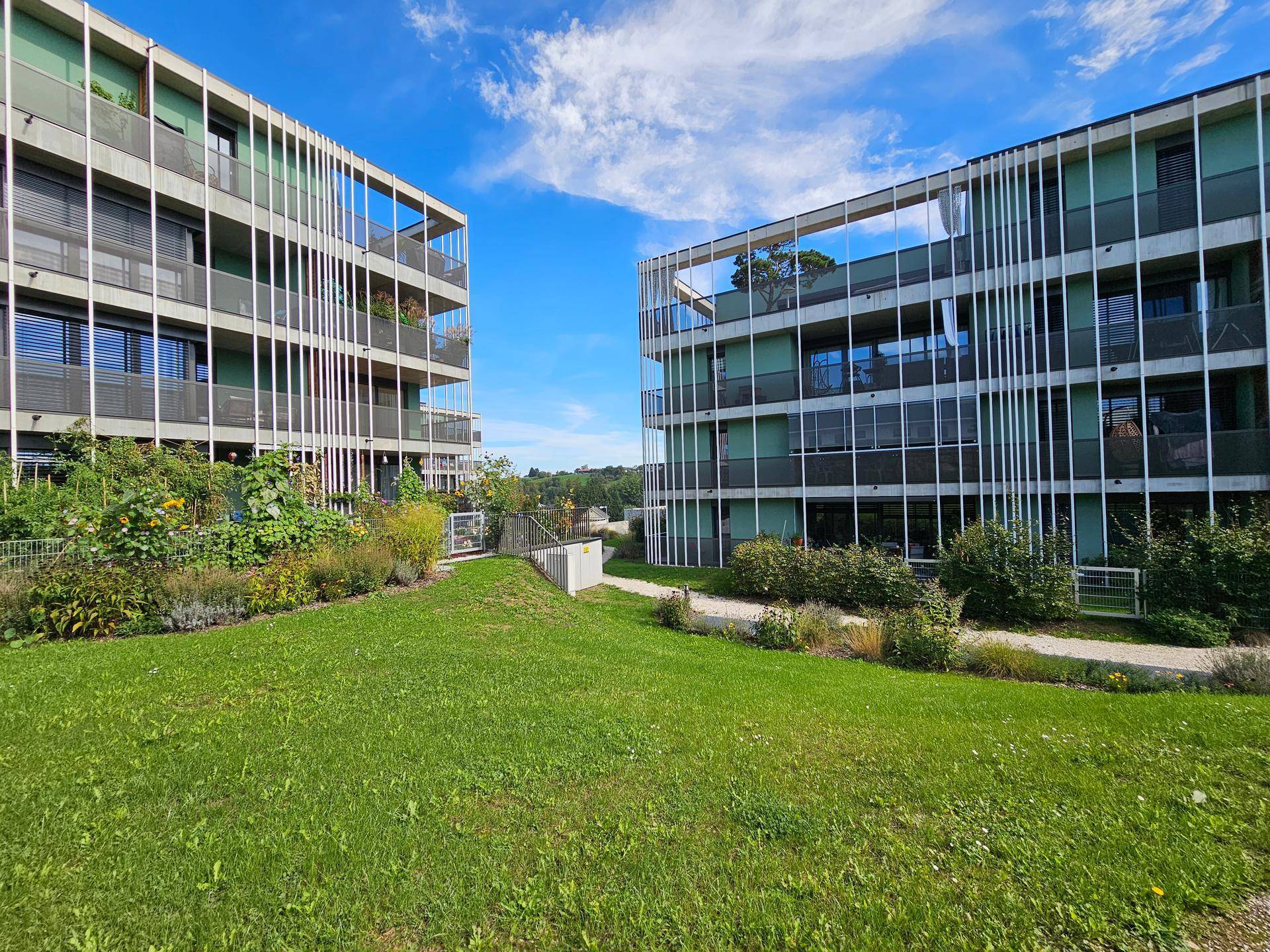 Moderne Wohngebäude umgeben von einer gepflegten Grünanlage unter blauem Himmel.