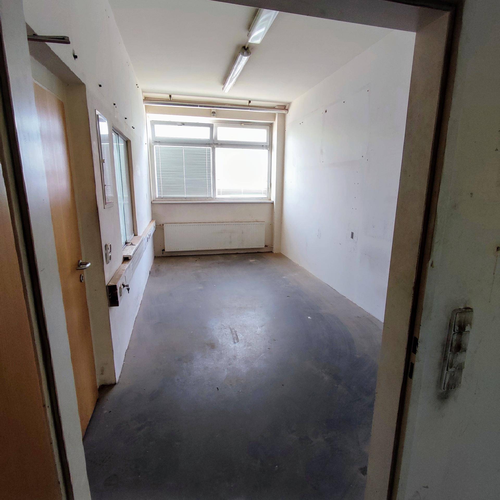 Kleiner, leerer Büroraum mit Betonboden, Fenster und Heizkörper unter der Fensterbank.