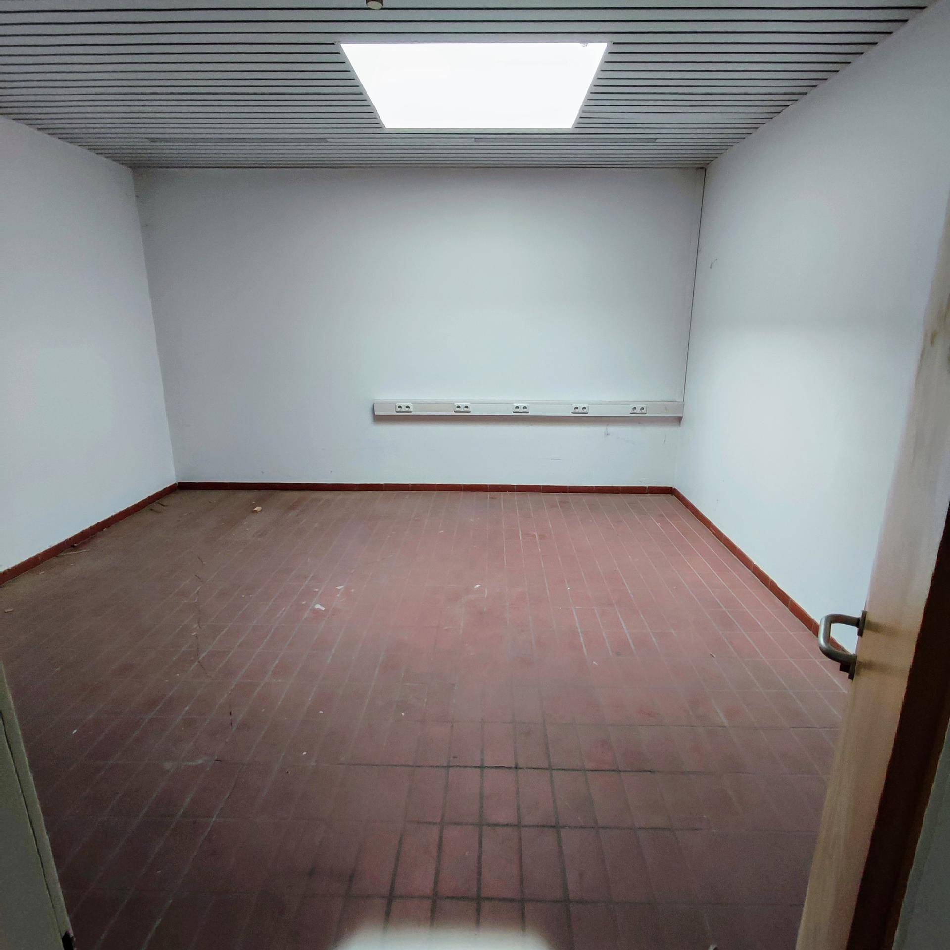 Leerer Büroraum mit roten Bodenfliesen, weißen Wänden und einer Deckenleuchte.
