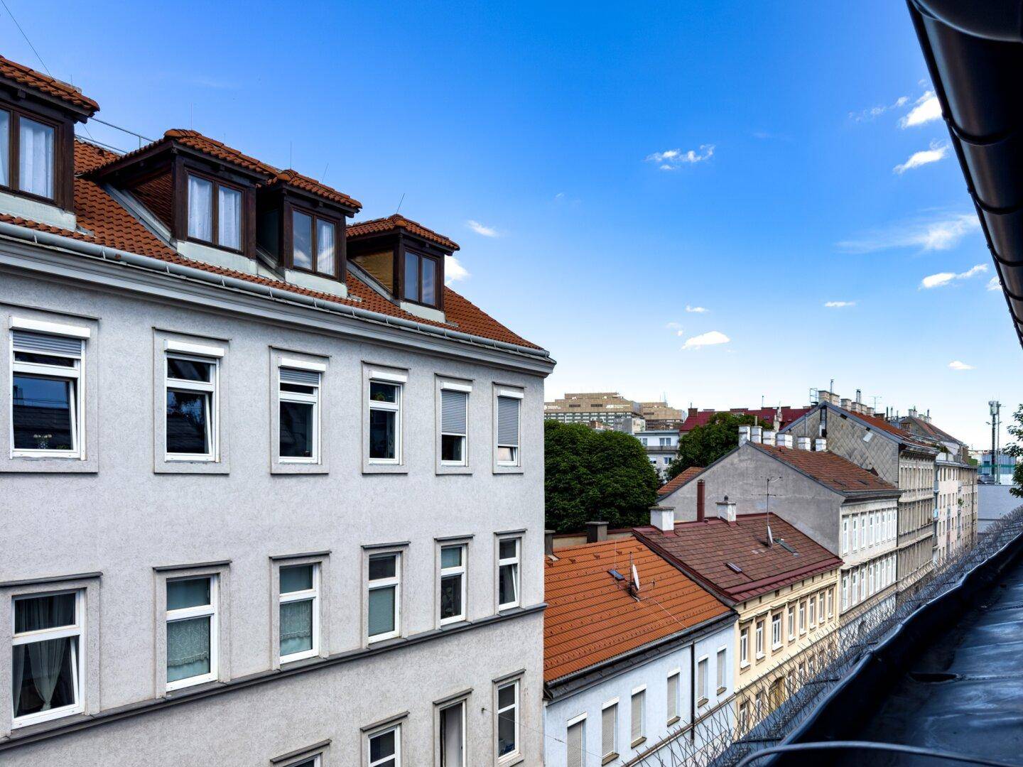 Blick auf eine Reihe von Wohngebäuden mit roten Ziegeldächern und Dachgauben unter blauem Himmel.