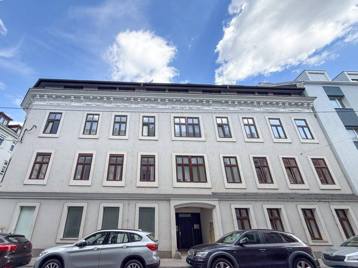 Fassade eines mehrstöckigen Wohngebäudes von der Straße aus gesehen, mit geparkten Autos.