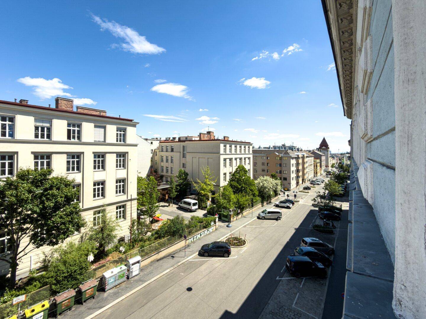 Panoramablick über eine belebte Stadtstraße mit historischen Gebäuden und viel Grün.