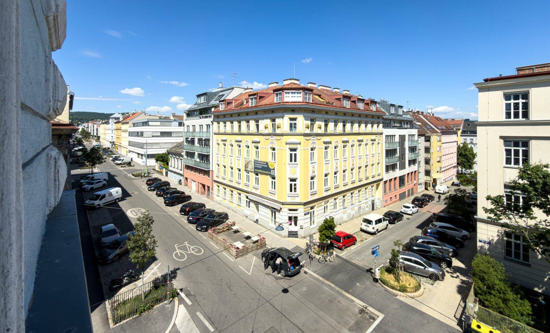 Weitläufiger Blick über eine städtische Kreuzung mit historischen Gebäuden und viel Verkehr.
