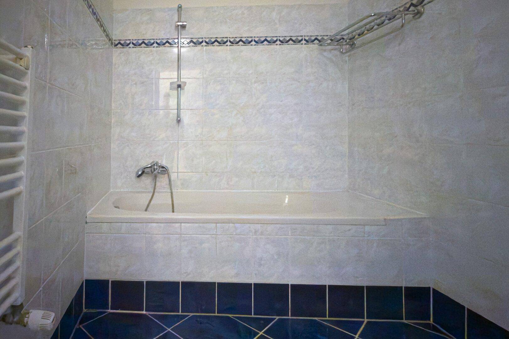 Badezimmer mit eingebauter Badewanne, gefliesten Wänden und einem Handtuchheizkörper.