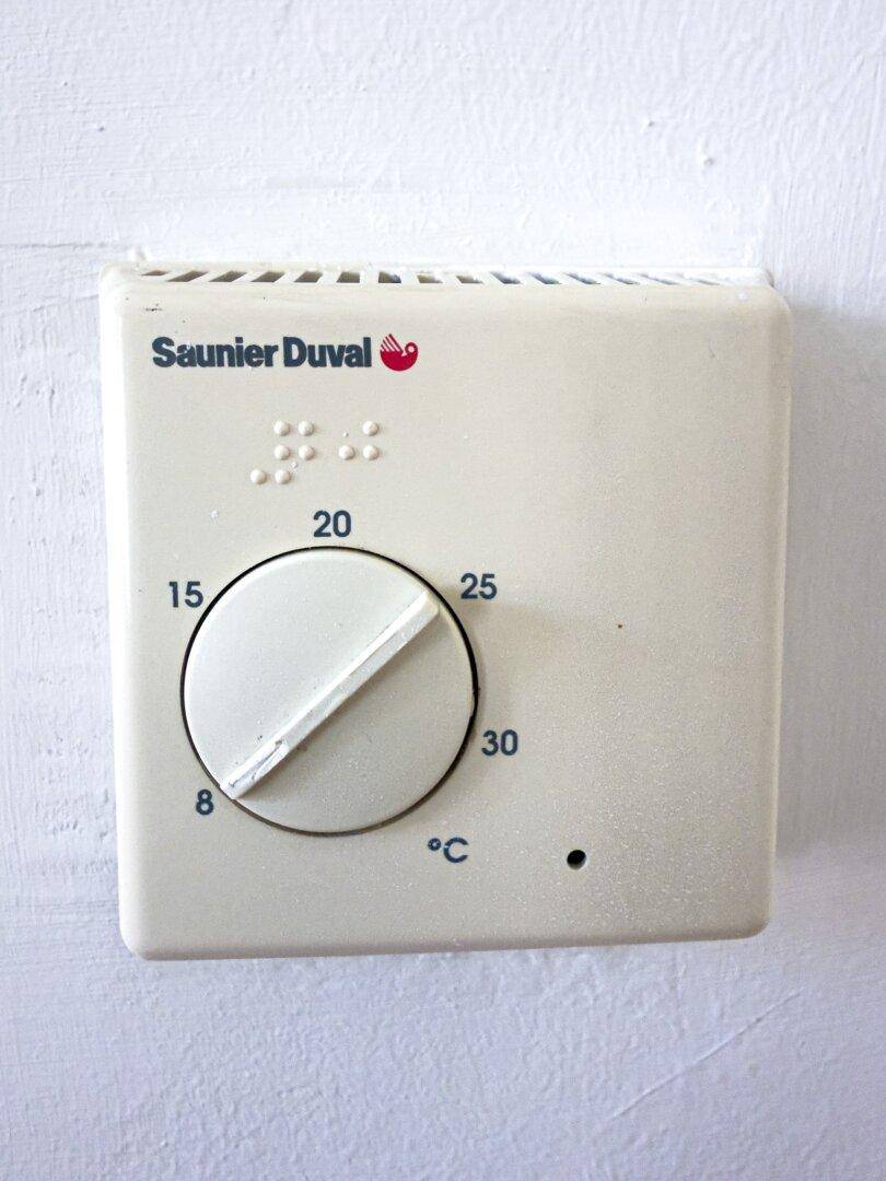 Nahaufnahme eines älteren Thermostats an einer weißen Wand zur Temperaturregelung.
