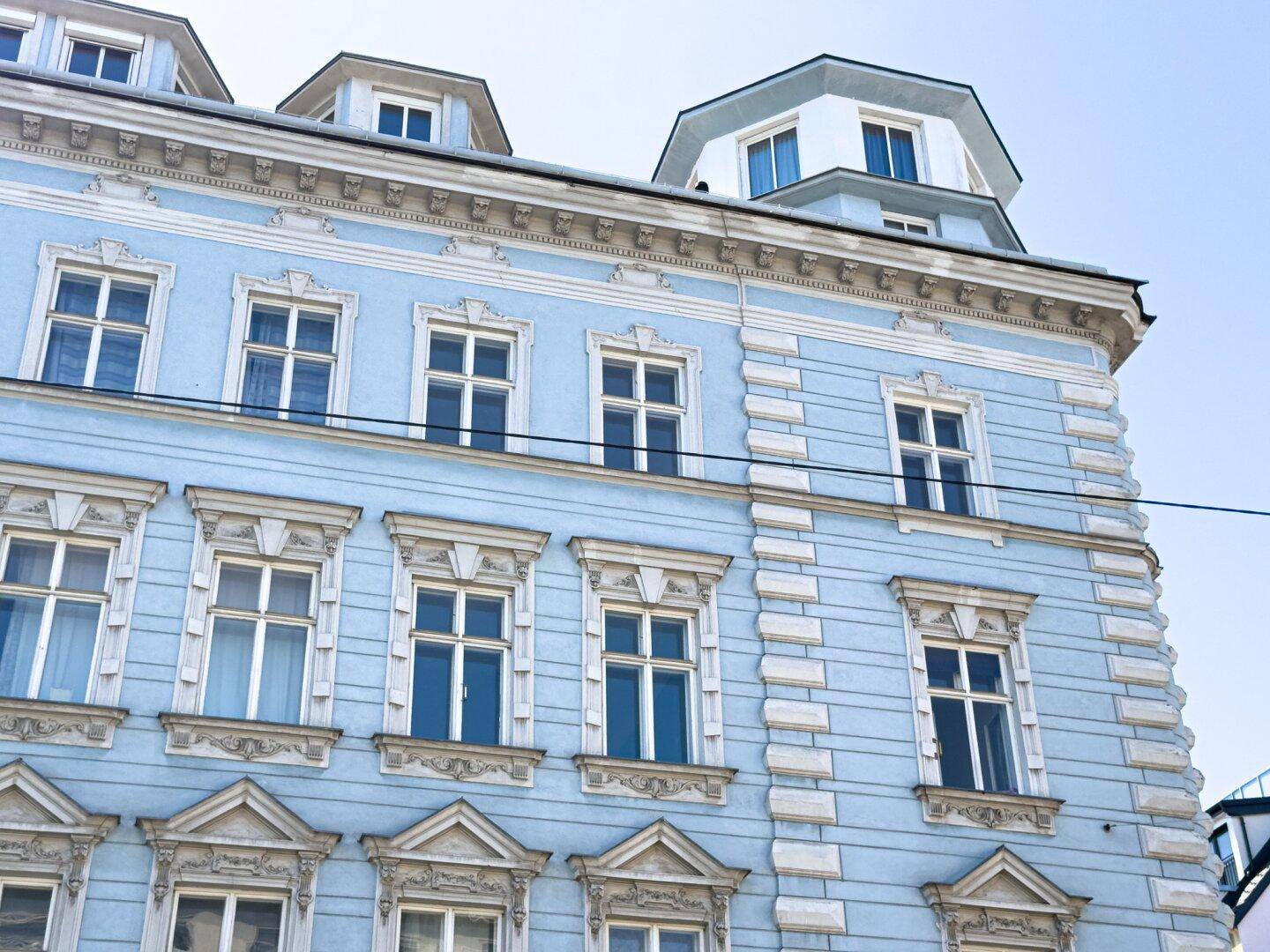 Historische Fassade eines Altbaus in Hellblau mit aufwendigen Stuckverzierungen und Dachgauben.