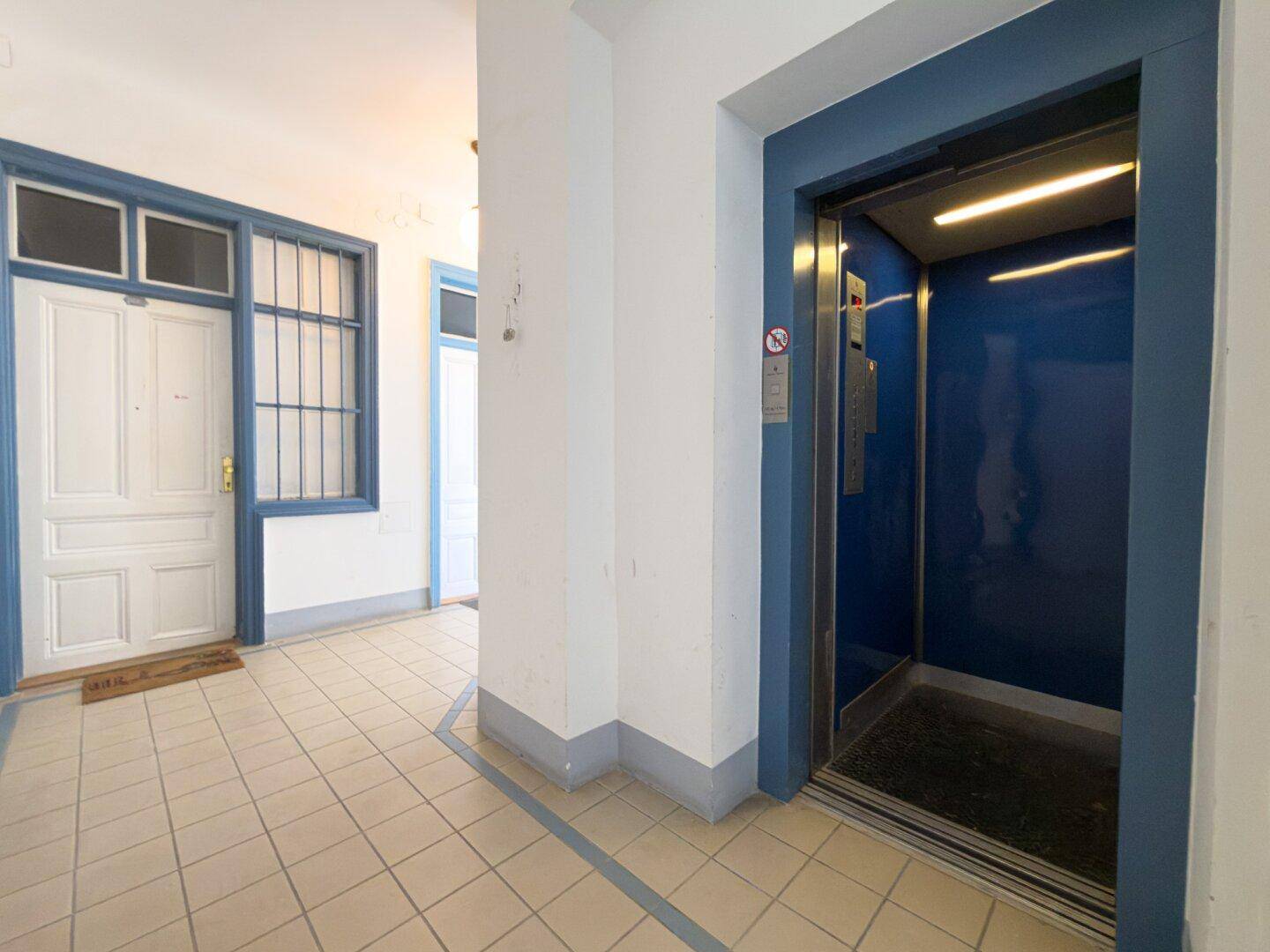 Heller Eingangsbereich mit Fliesenboden und einem modernen Aufzug, der Zugang zu den Etagen bietet.