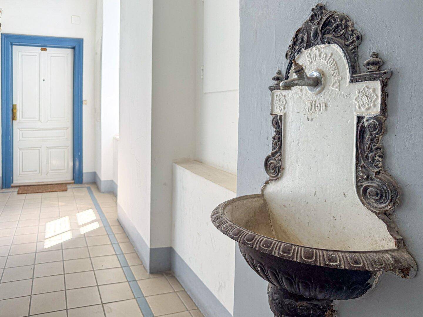 Eingangsbereich mit Fliesenboden, einem dekorativen Wandbrunnen und einer blauen Tür.