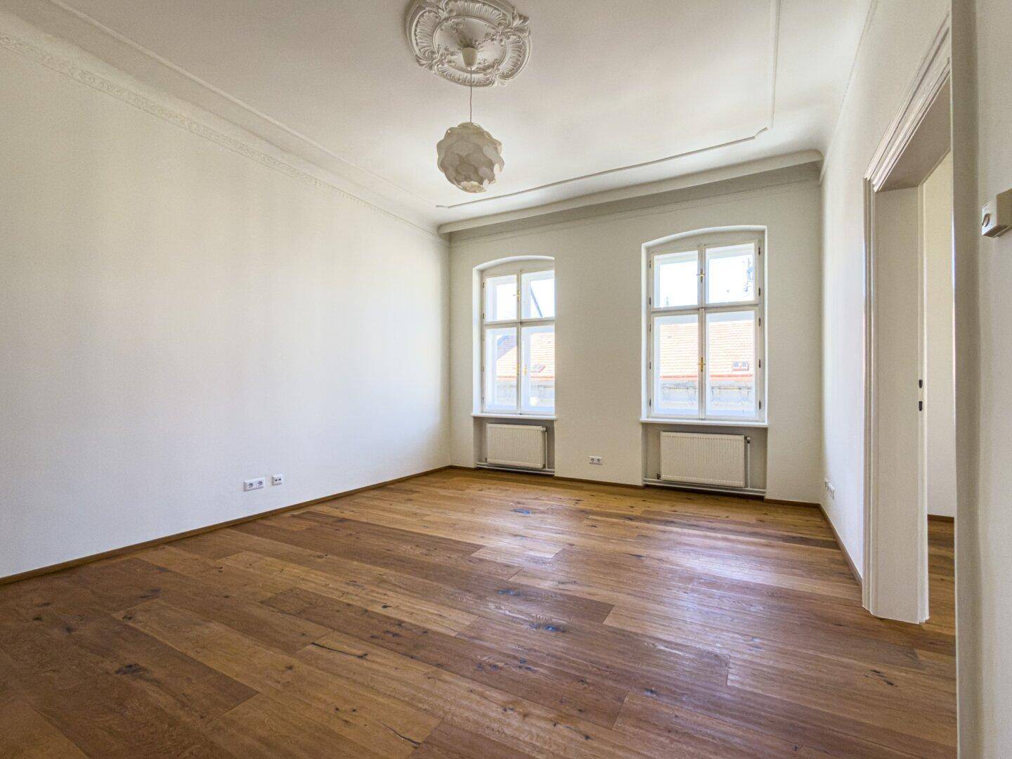 Geräumiges Zimmer mit Parkettboden und zwei Fenstern, bietet viel Tageslicht und eine offene Gestaltung.