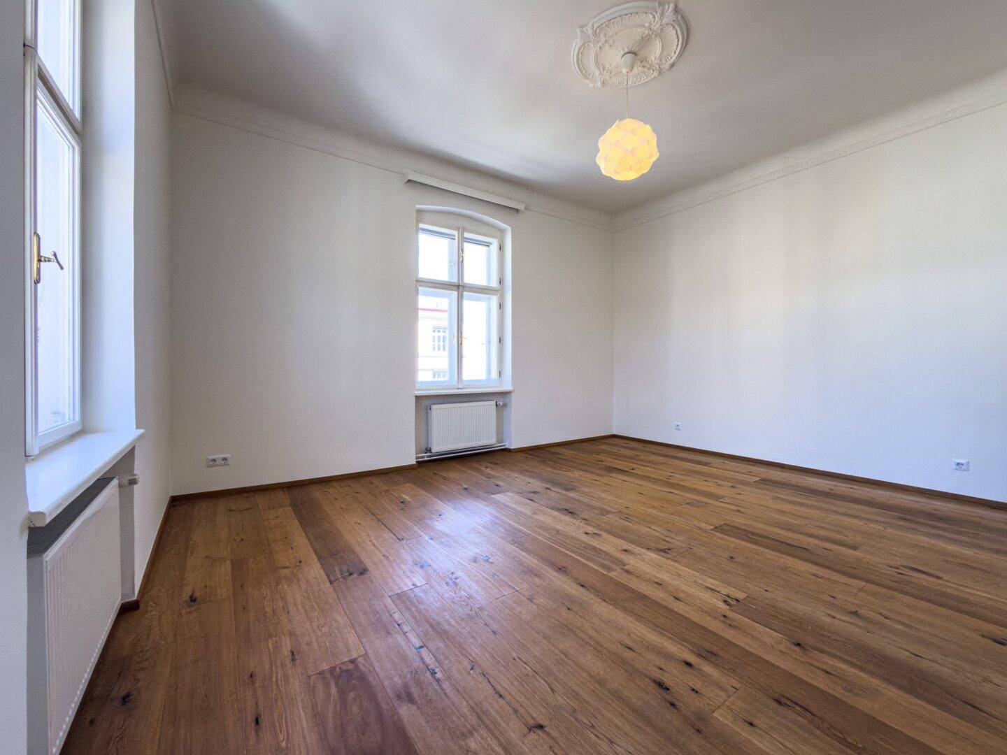 Geräumiges Zimmer mit Parkettboden, hohen Decken und Stuckverzierung, bietet viel natürliches Licht.