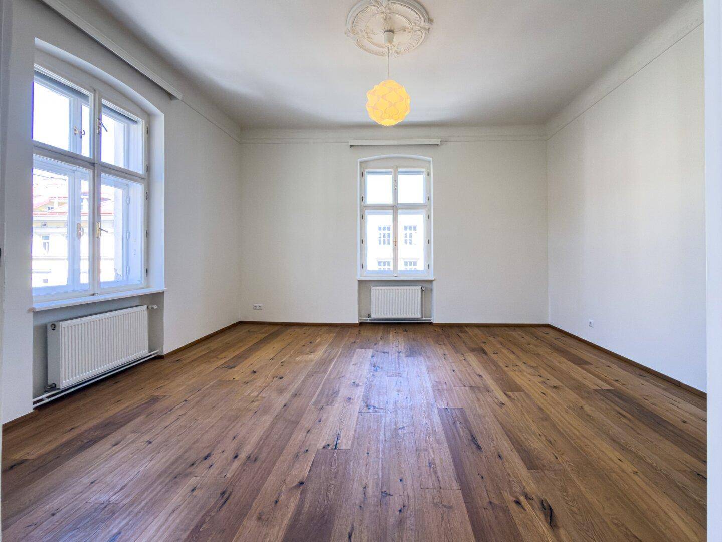 Geräumiges Zimmer mit hellem Parkettboden, hohen Decken und klassischem Stuck, bietet viel Tageslicht.