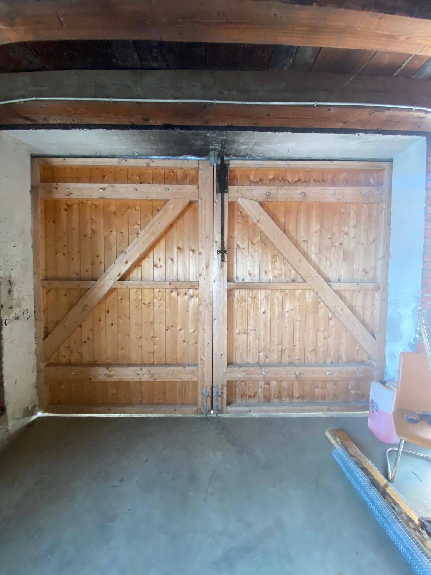 Innenansicht eines Lagerraums mit großen Holztüren und sichtbaren Deckenbalken aus Holz.