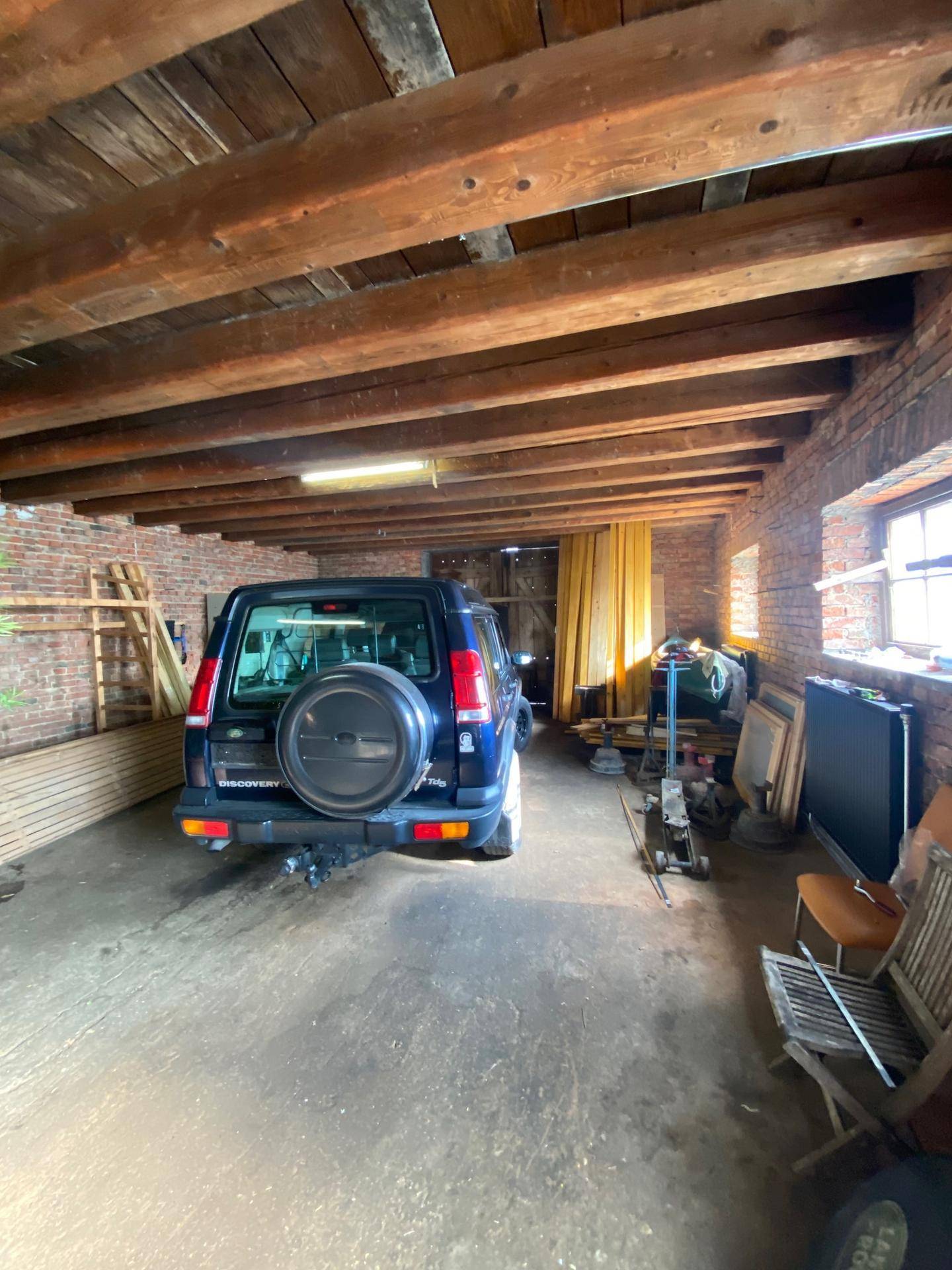 Geräumiger Lagerraum mit einem geparkten Auto, sichtbaren Holzbalken und Ziegelwänden.