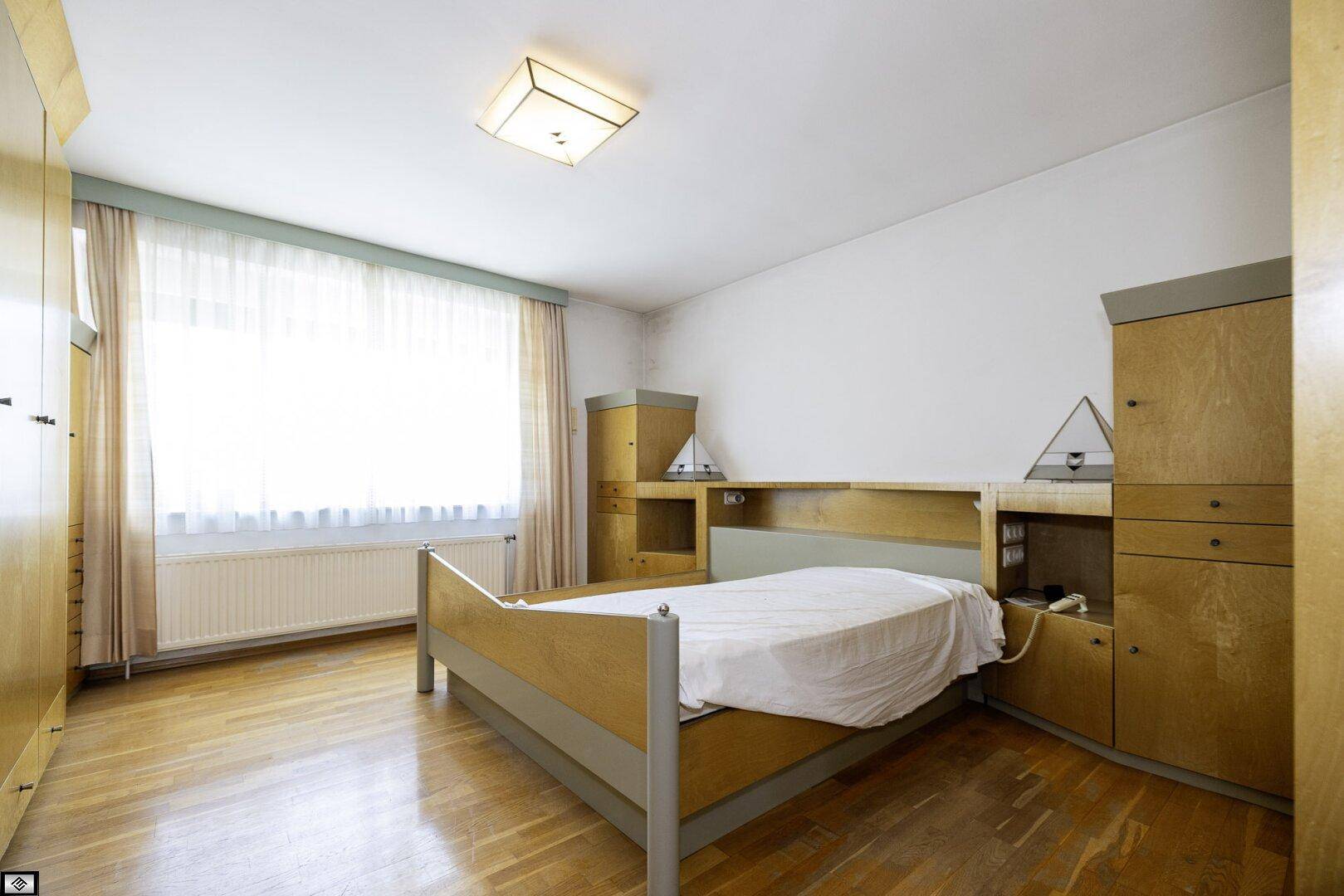 Schlafzimmer mit Holzboden, großem Fenster und integrierten Holzschränken.