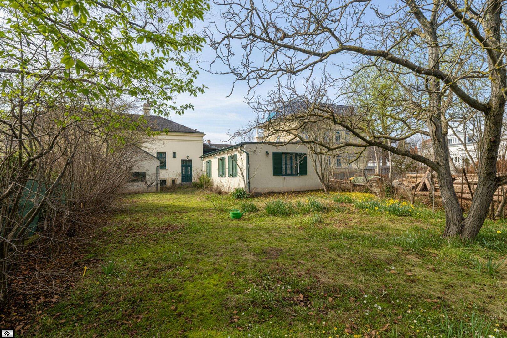 Großer, naturbelassener Garten mit Rasenfläche, altem Baumbestand und Blick auf die Rückseite des Hauses.