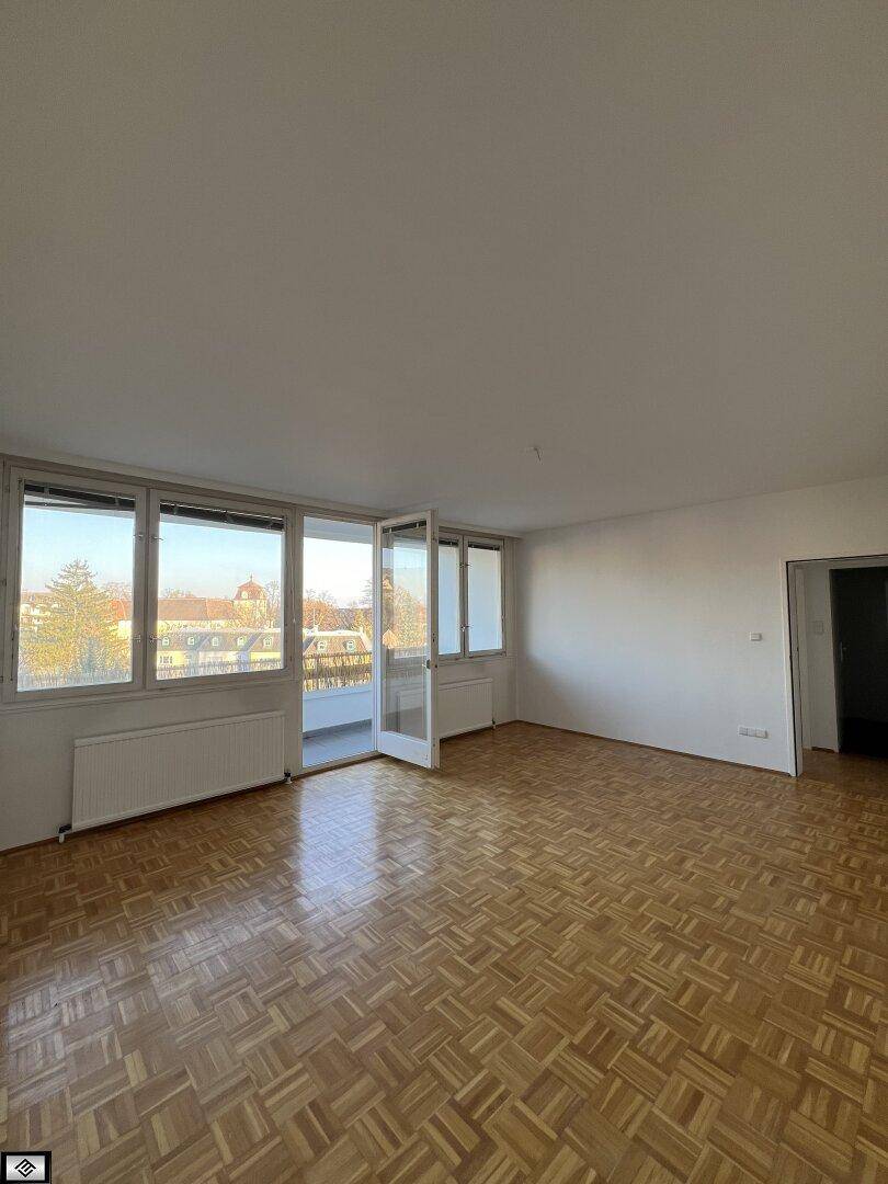 Helles Wohnzimmer mit Fischgrätparkett und Zugang zu einem sonnigen Balkon.