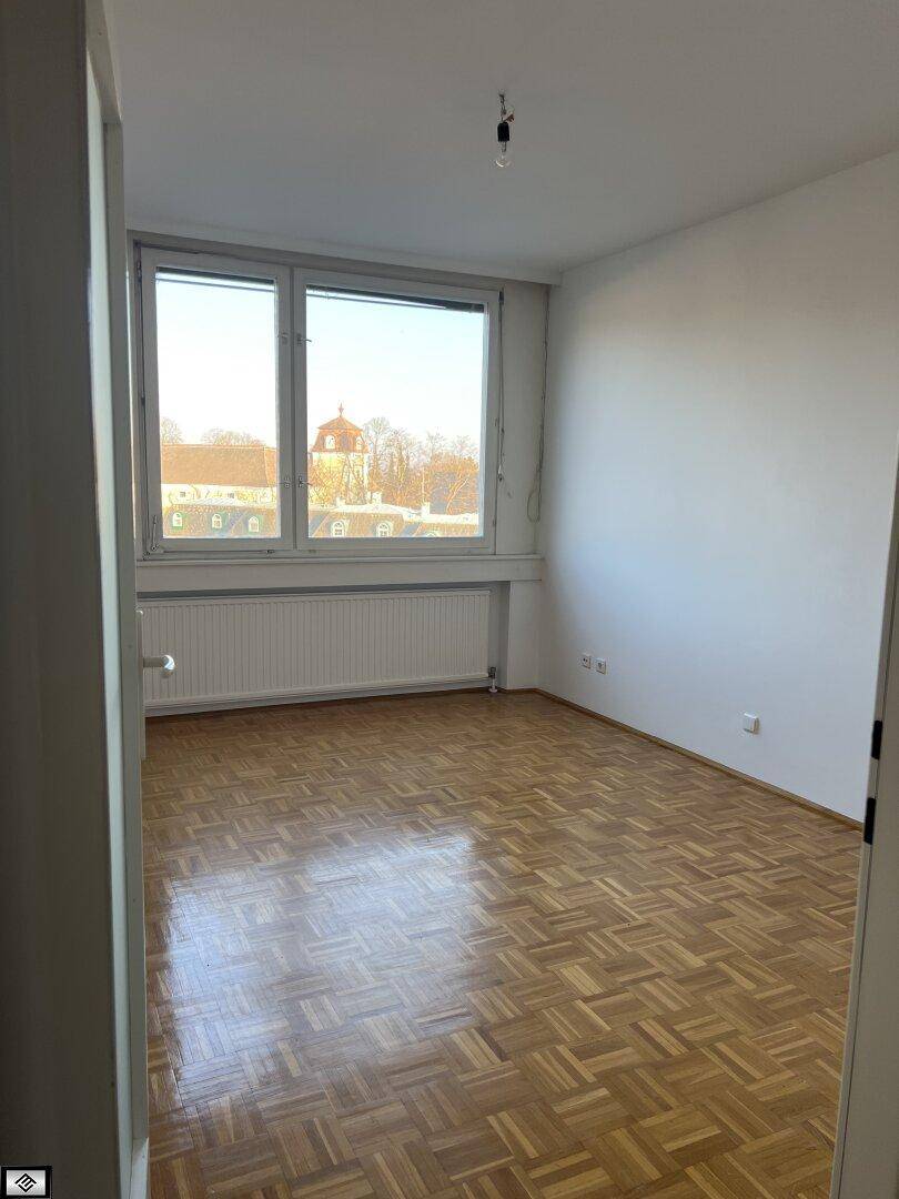 Helles Schlafzimmer mit Parkettboden und großem Fenster, das viel Licht hereinlässt.