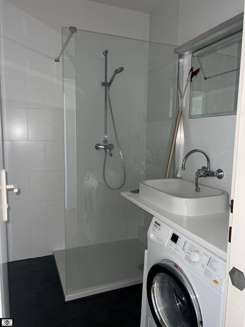 Modernes Badezimmer mit ebenerdiger Dusche, Waschbecken und integrierter Waschmaschine.