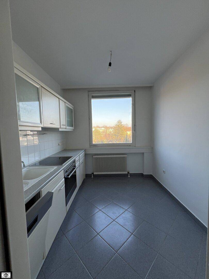 Funktionale Küche mit weißen Schränken, grauen Fliesen und Fenster mit Ausblick.