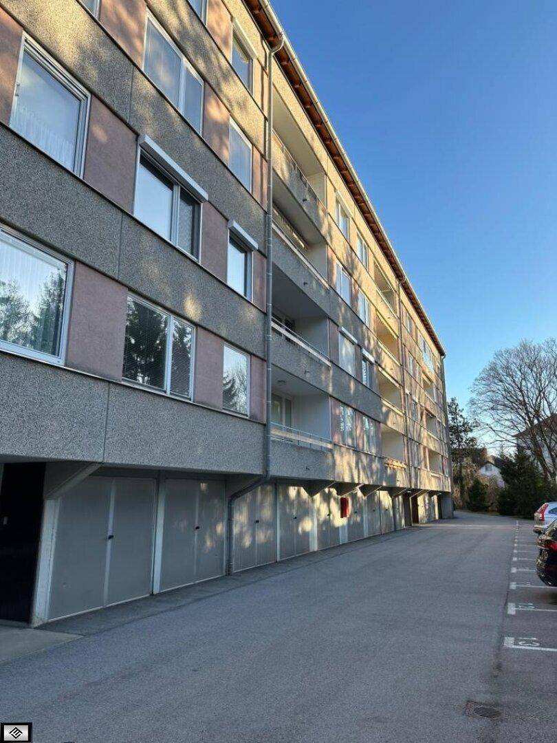 Mehrfamilienhaus mit Balkonen und Garagen im Erdgeschoss, umgeben von Grünflächen.