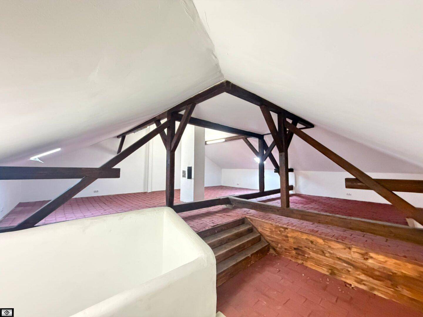 Geräumiger Dachboden mit sichtbaren Holzbalken und rotem Fliesenboden, ideal für Ausbau.