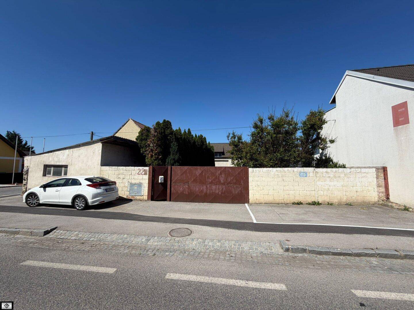 Ansicht des Grundstücks von der Straße mit einem großen Tor und einem geparkten Auto.