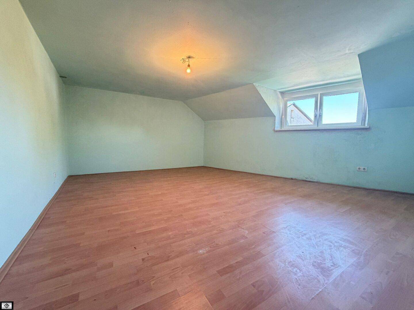 Helles Zimmer im Dachgeschoss mit hellgrünen Wänden, Laminatboden und einem Fenster.